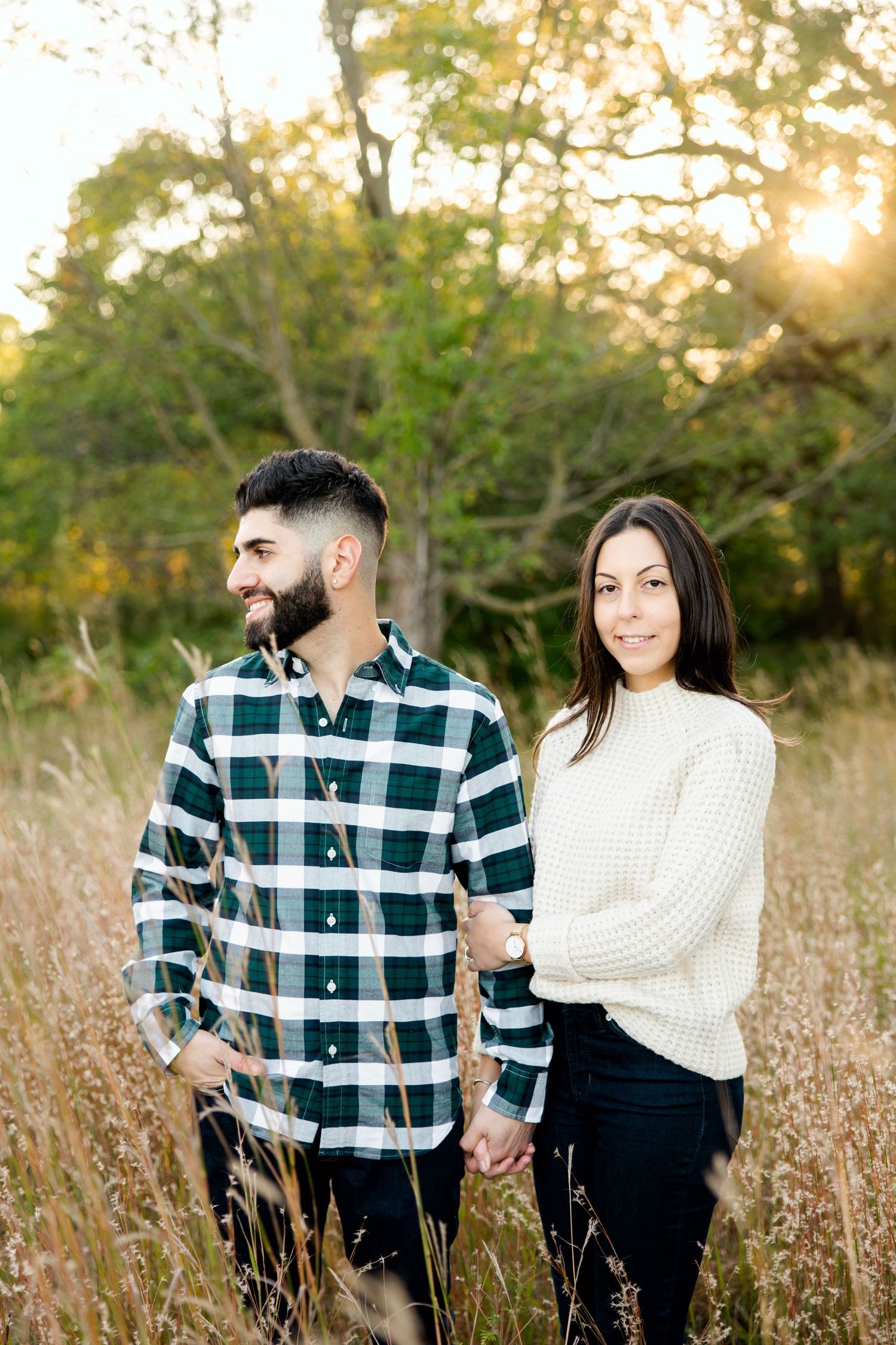 Couple in coordinated sweaters poses among tall grass during golden hour.