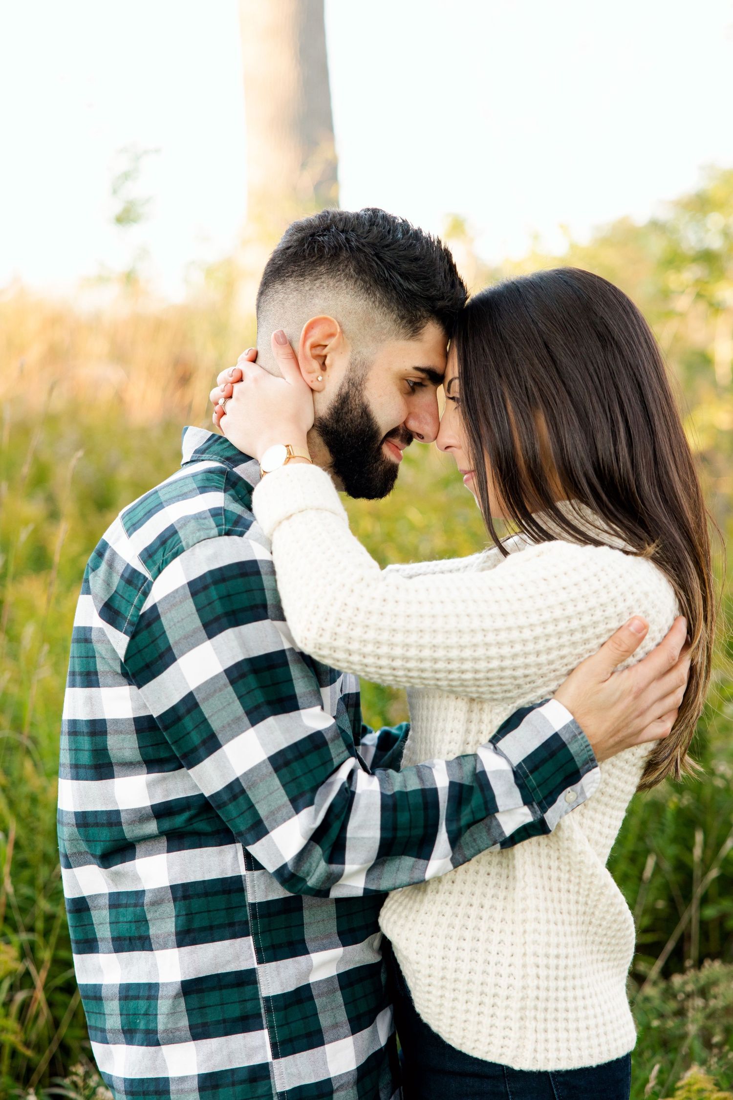 Couple in cozy sweaters share intimate moment outdoors during golden hour in fall field.