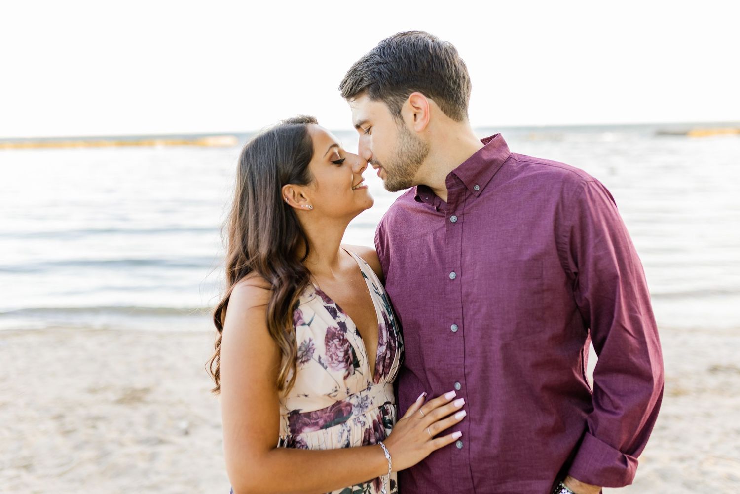 A tender moment between a couple on a beach with sunlit water behind them.