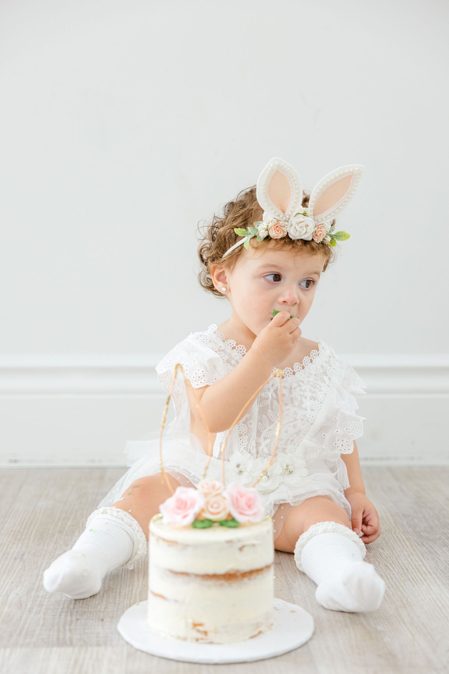 Adorable spring portrait with white dress and bunny ear crown while tasting cake.