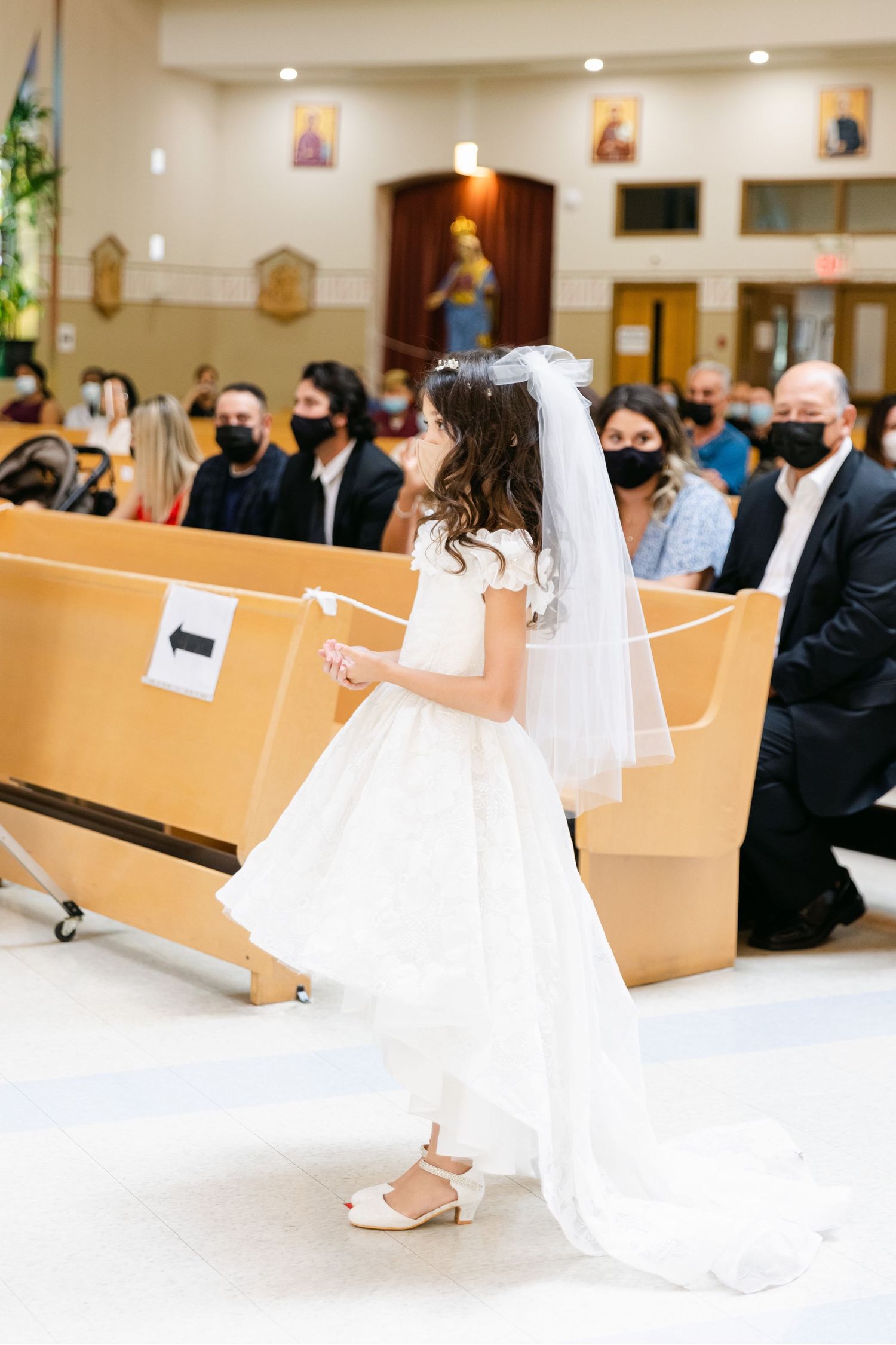 First communion ceremony in church with attendees wearing masks in pews.