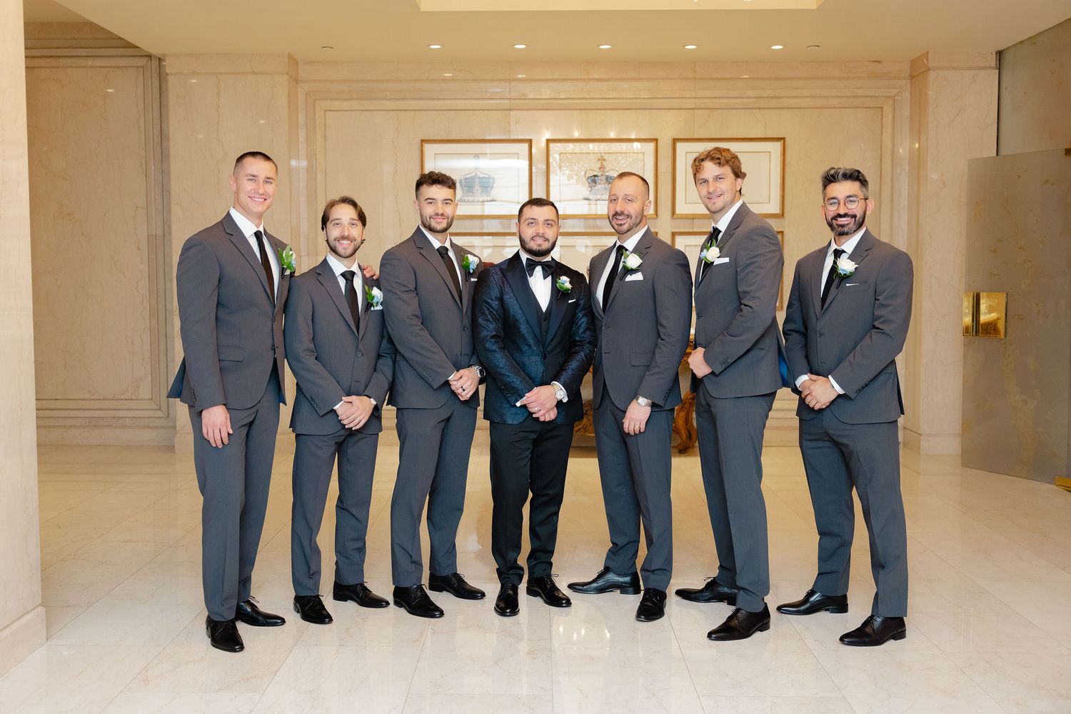 Wedding party members in navy suits and gray dresses pose together in an elegant indoor venue.