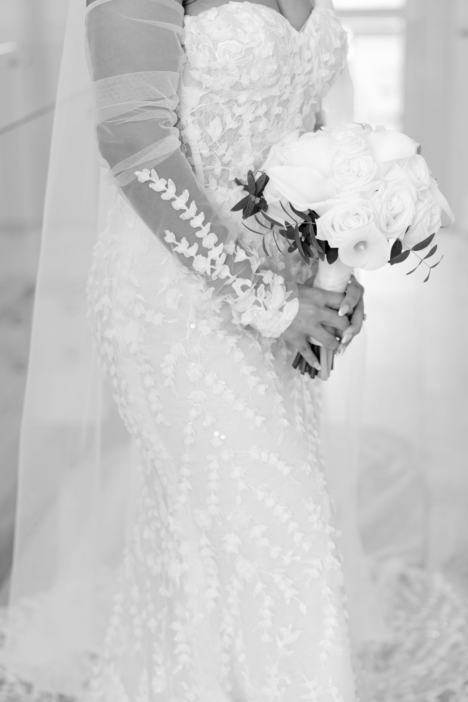 Black and white detail shot of lace wedding dress and white bouquet.