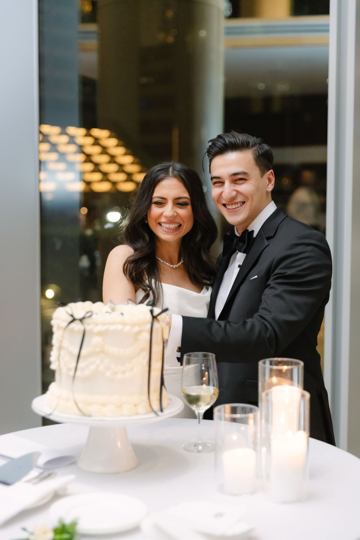 Newlyweds smiling together behind their elegant white wedding cake with candles.