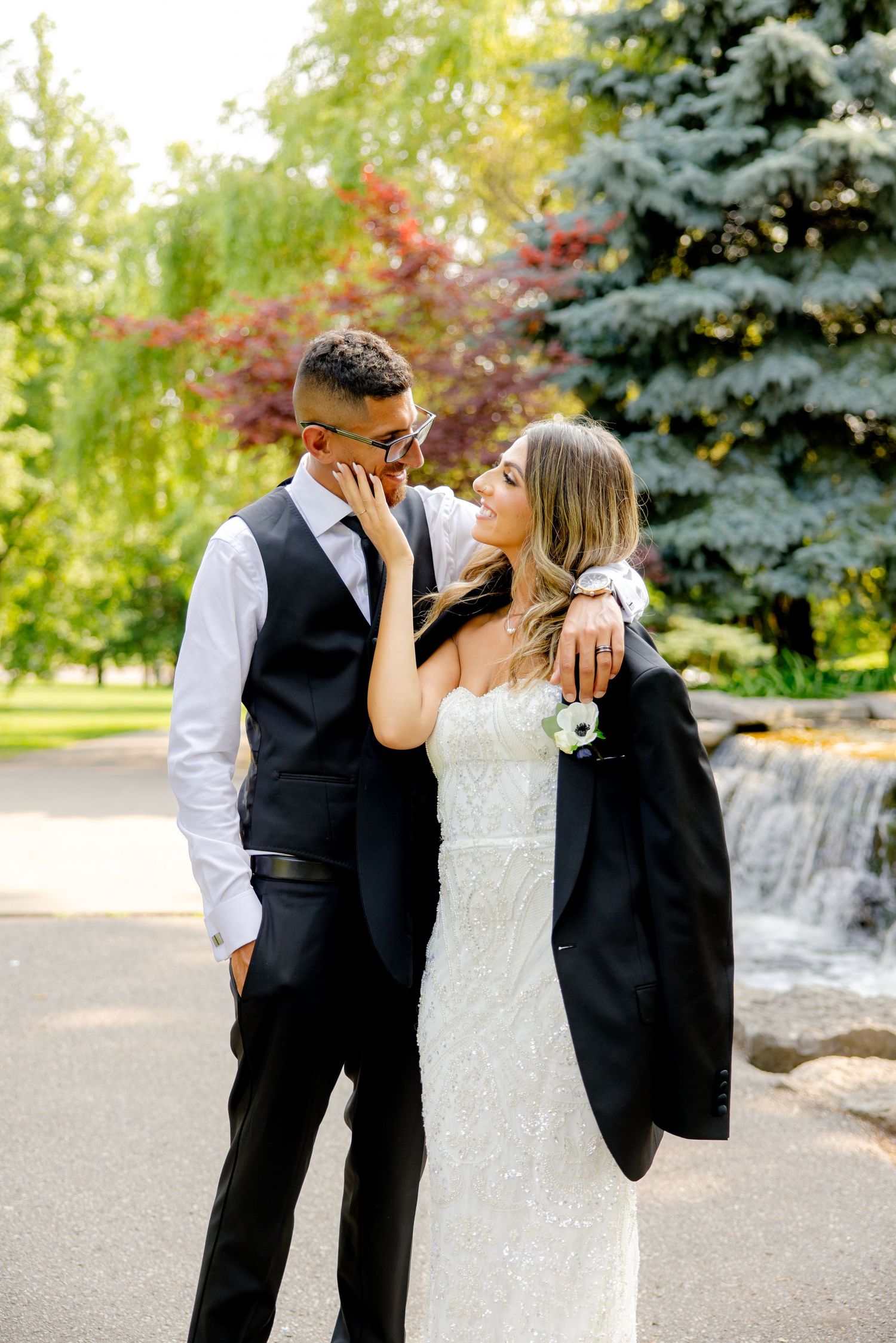 Romantic wedding photo near cascading waterfall with lush garden backdrop.