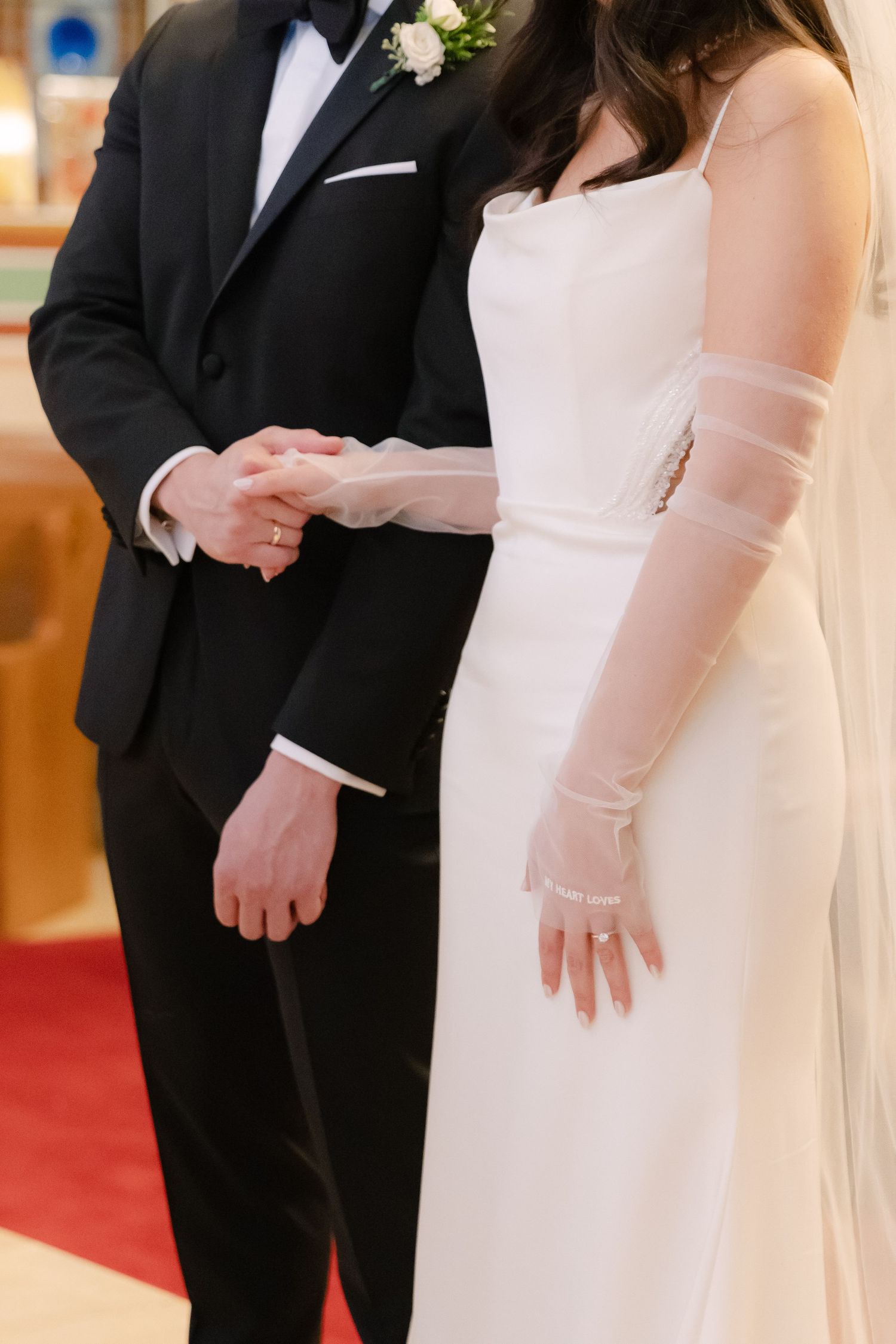 Close-up of wedding ceremony showing elegant white dress details and black tuxedo during ring exchange.