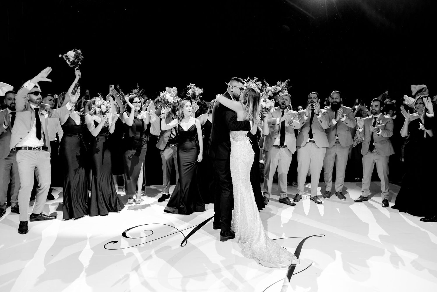 Black and white photo of couple's first dance surrounded by wedding guests taking photos.
