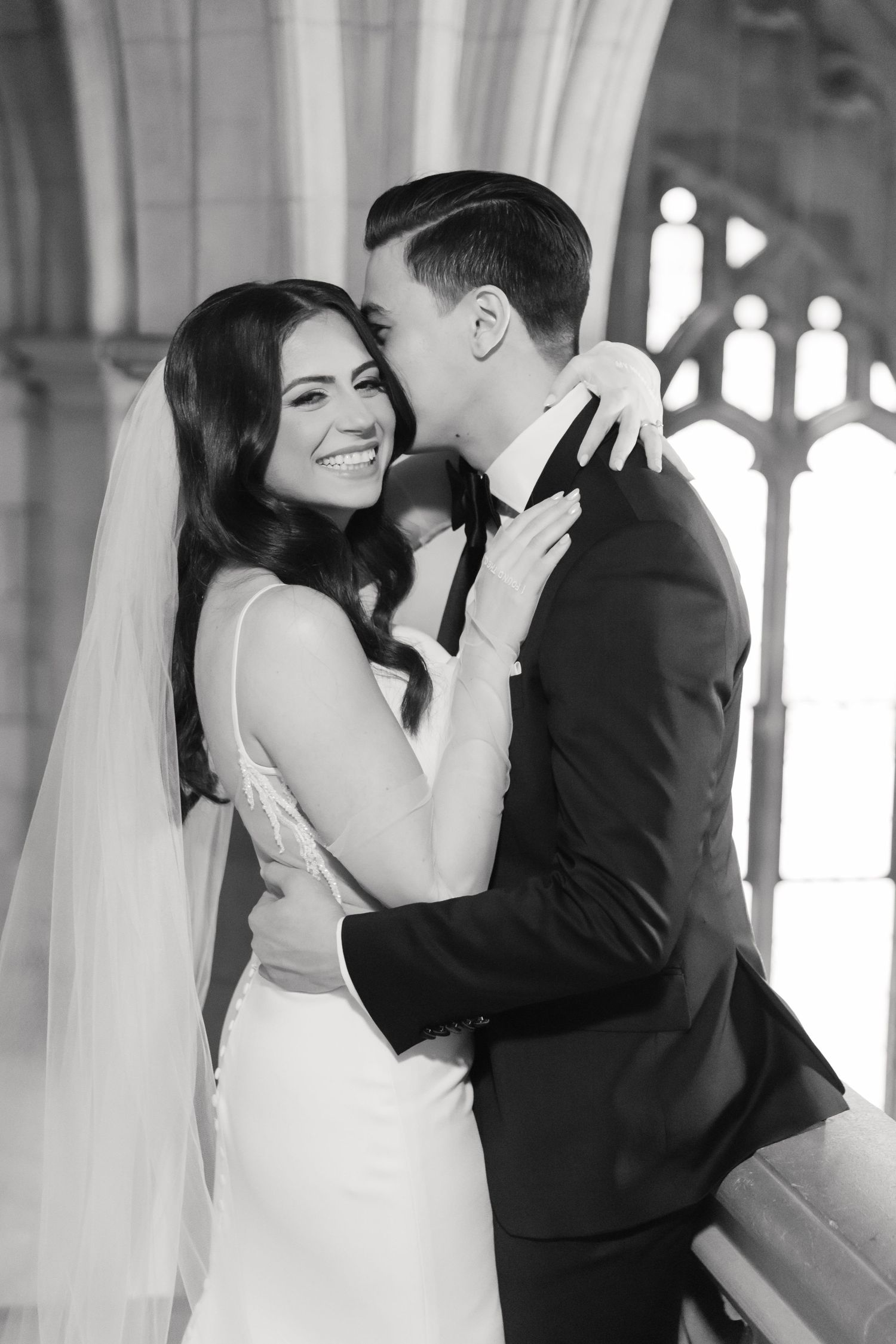 Joyful black and white wedding portrait under arched cathedral ceiling.