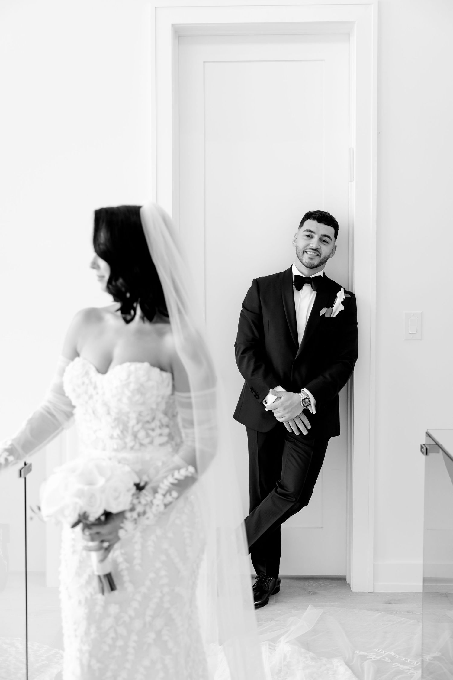 Black and white photo of bride and groom sharing playful moment in doorway.