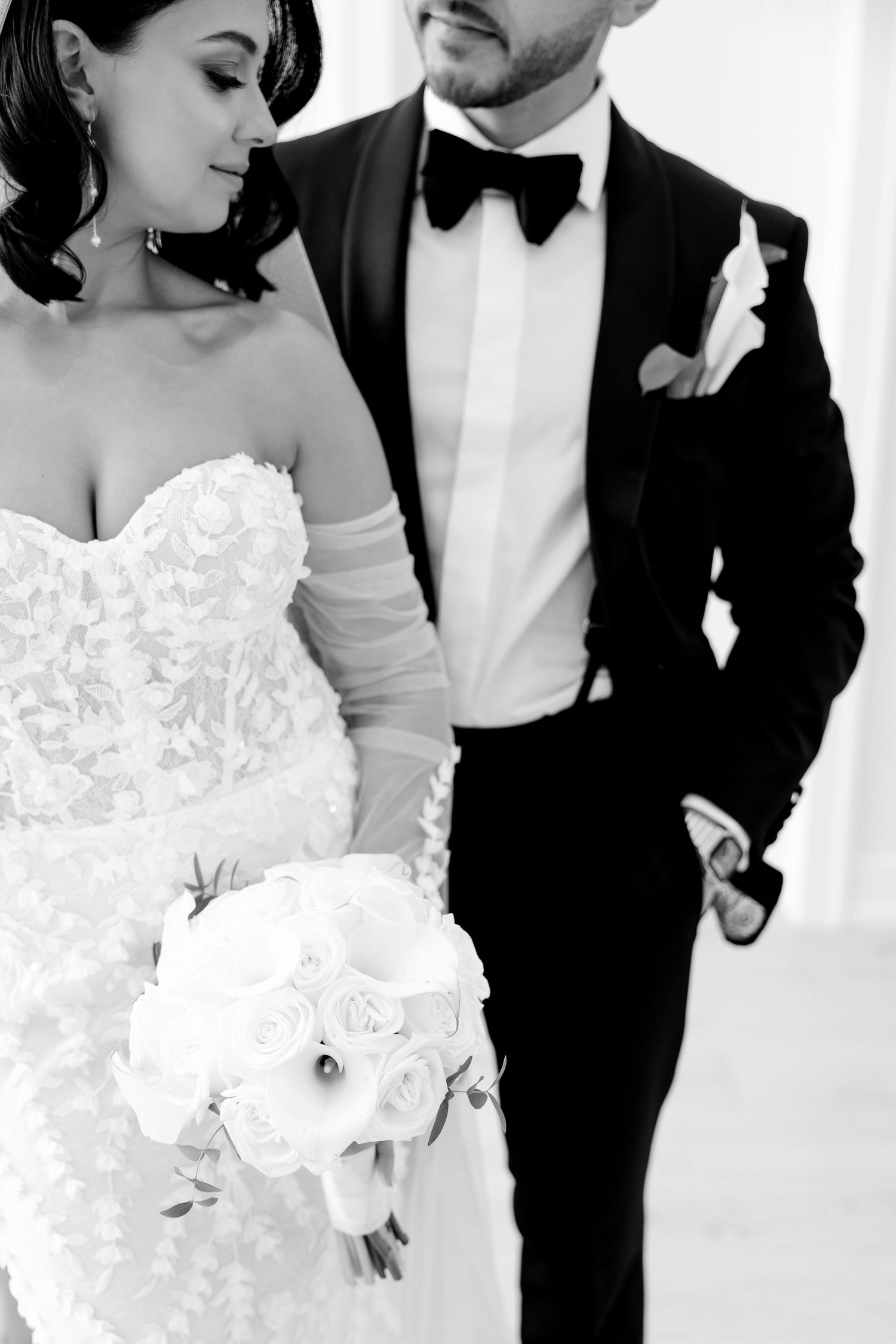 Black and white photo of newlyweds with focus on bride's lace dress and groom's bow tie.