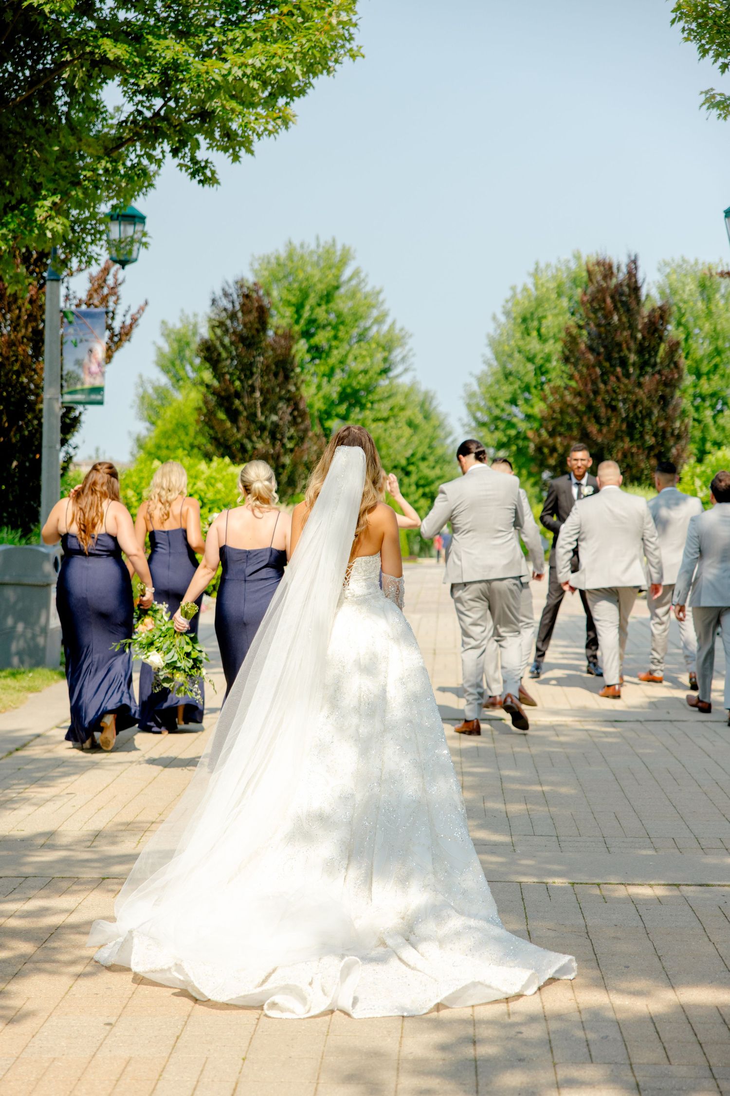 Wedding party walking on stone path with bride's flowing white dress train.