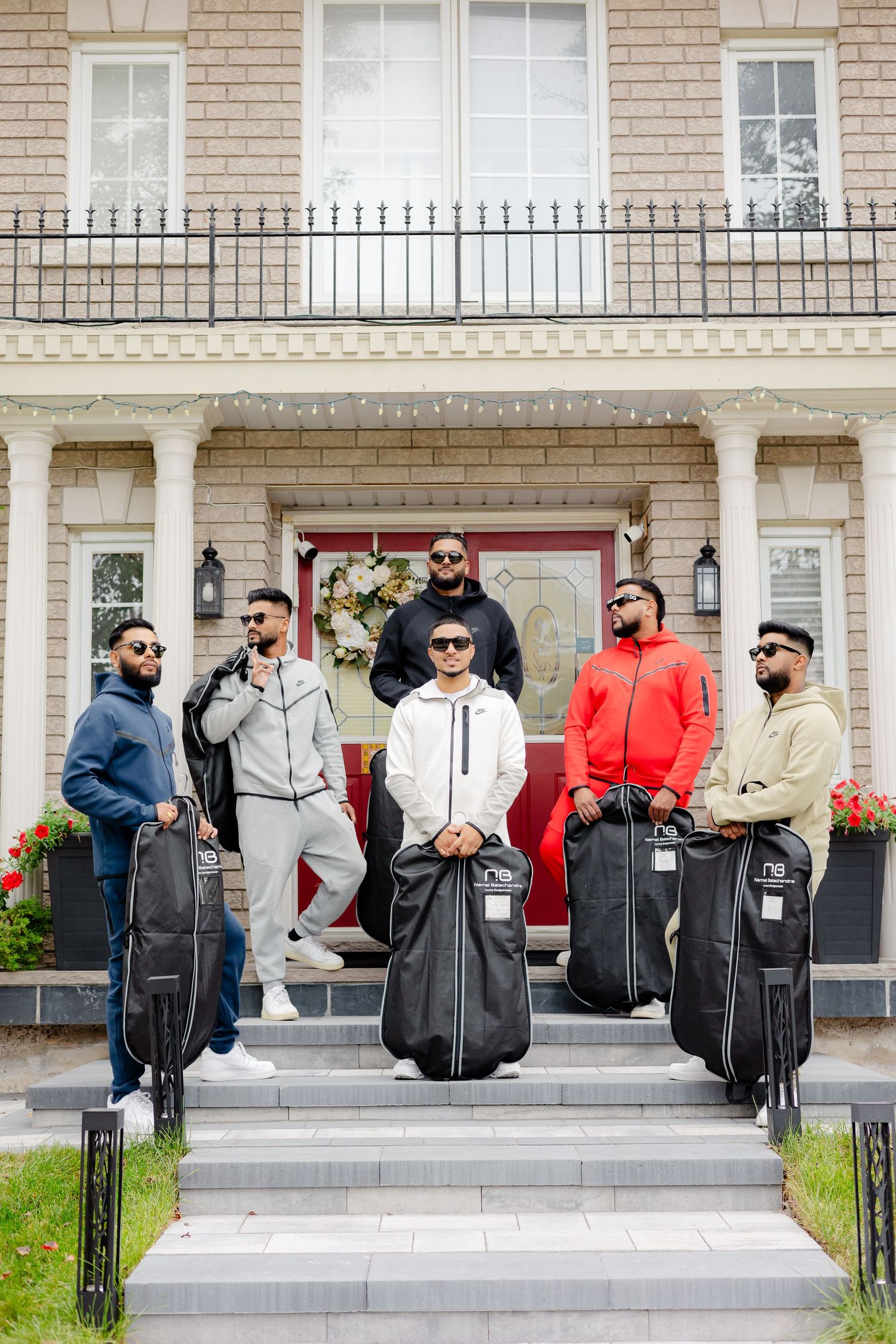 A group poses with garment bags on the front steps of a brick house with a red door.