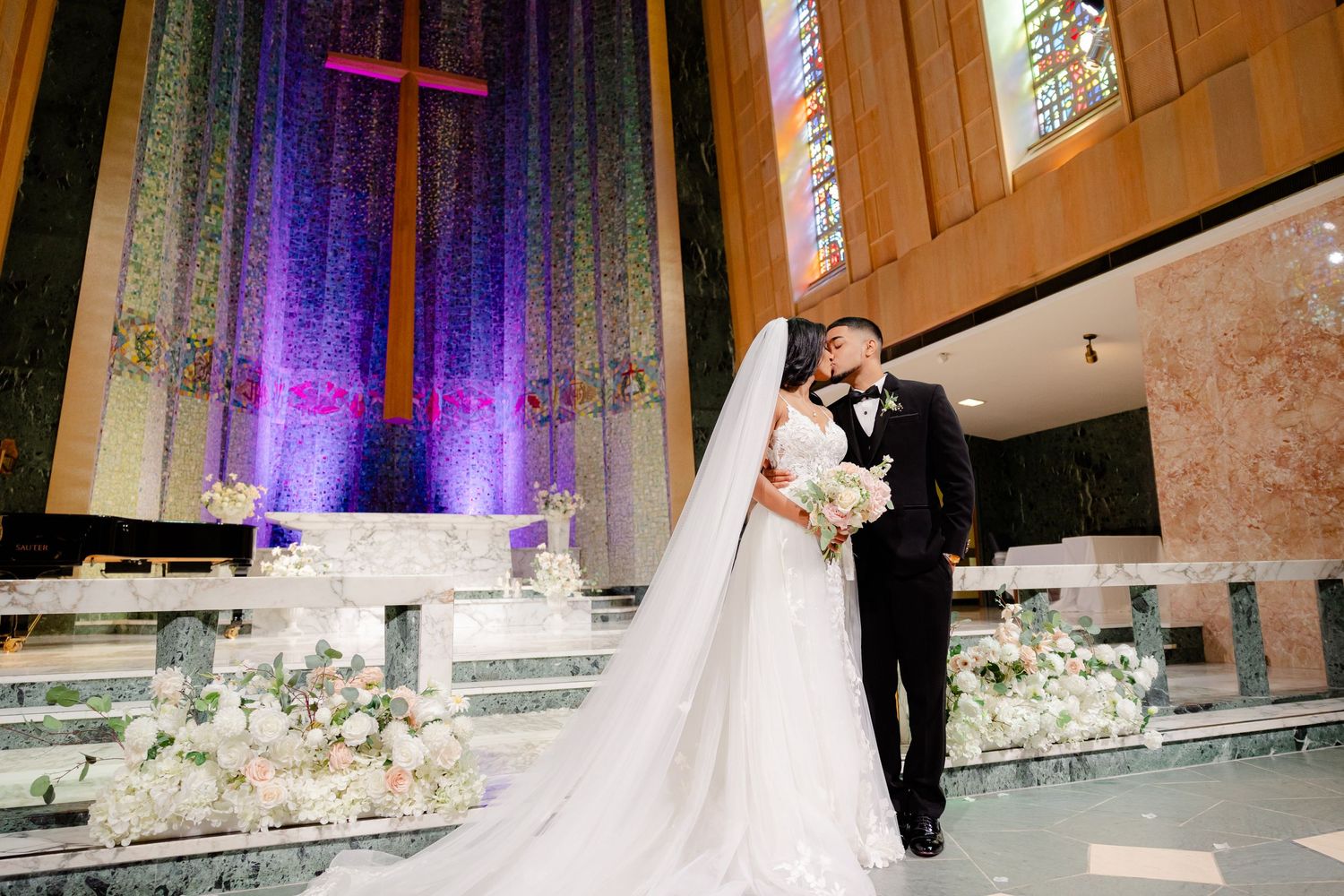 Wedding ceremony in front of illuminated cross and purple-lit altar.