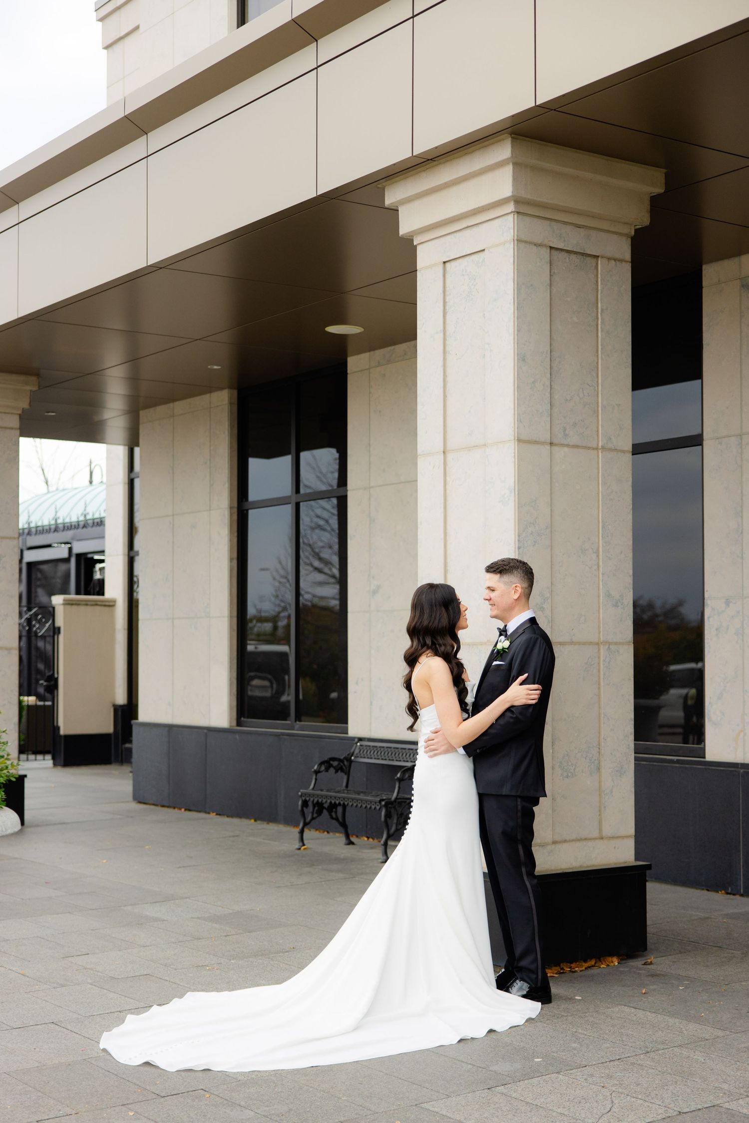Wedding couple poses under architectural columns with bride's dress train elegantly displayed.