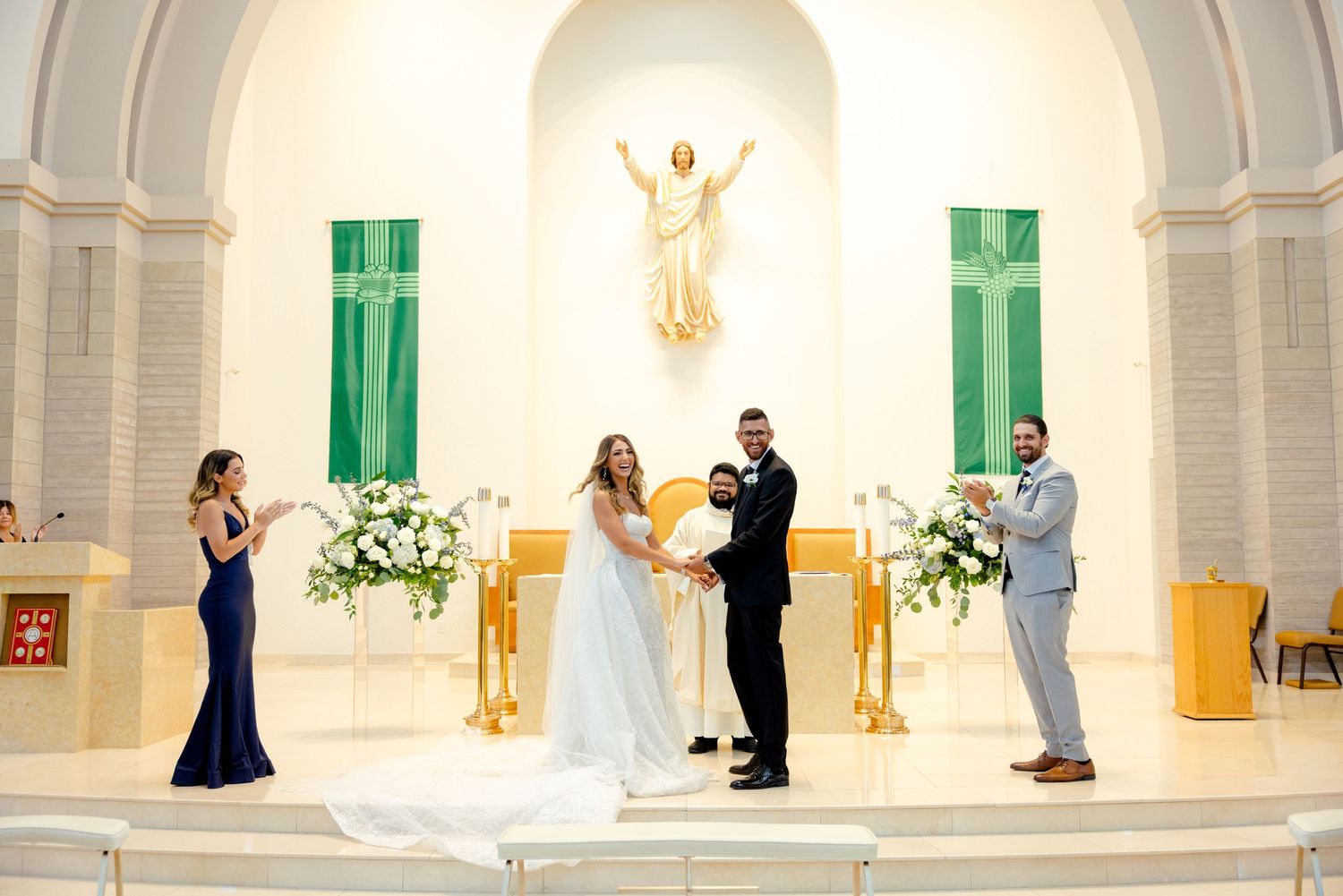 Intimate wedding ceremony in a bright church sanctuary with green banners and white floral arrangements.
