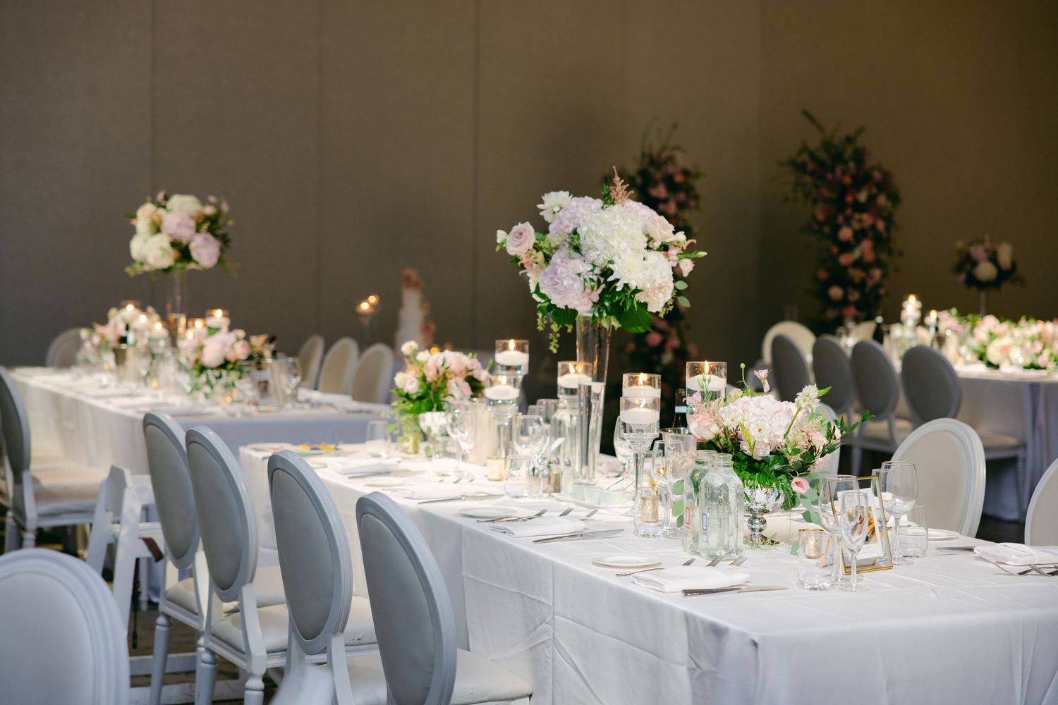 Long wedding reception table with white linens and floral centerpieces in an elegant ballroom setting.