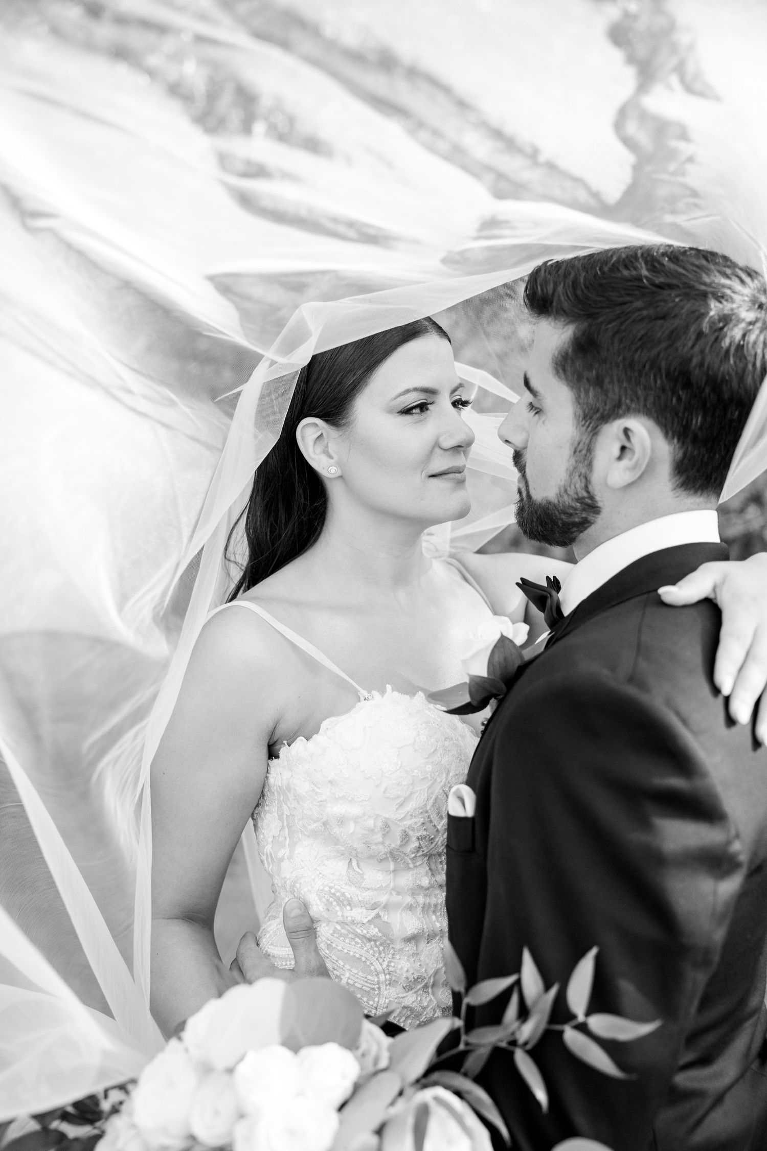 Black and white wedding photo captures an intimate moment between newlyweds with flowing veil.