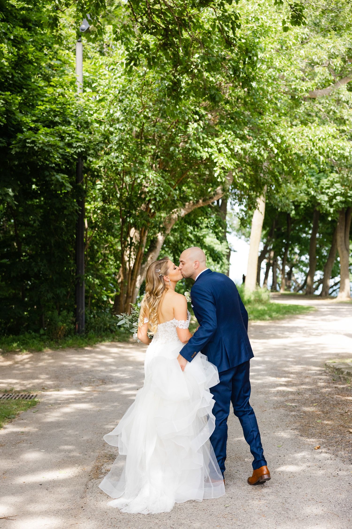 Romantic moment between newlyweds on wooded path with flowing white dress.