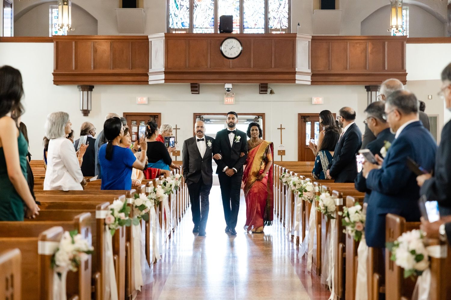 Church ceremony aisle decorated with floral arrangements and wooden pews filled with wedding guests.