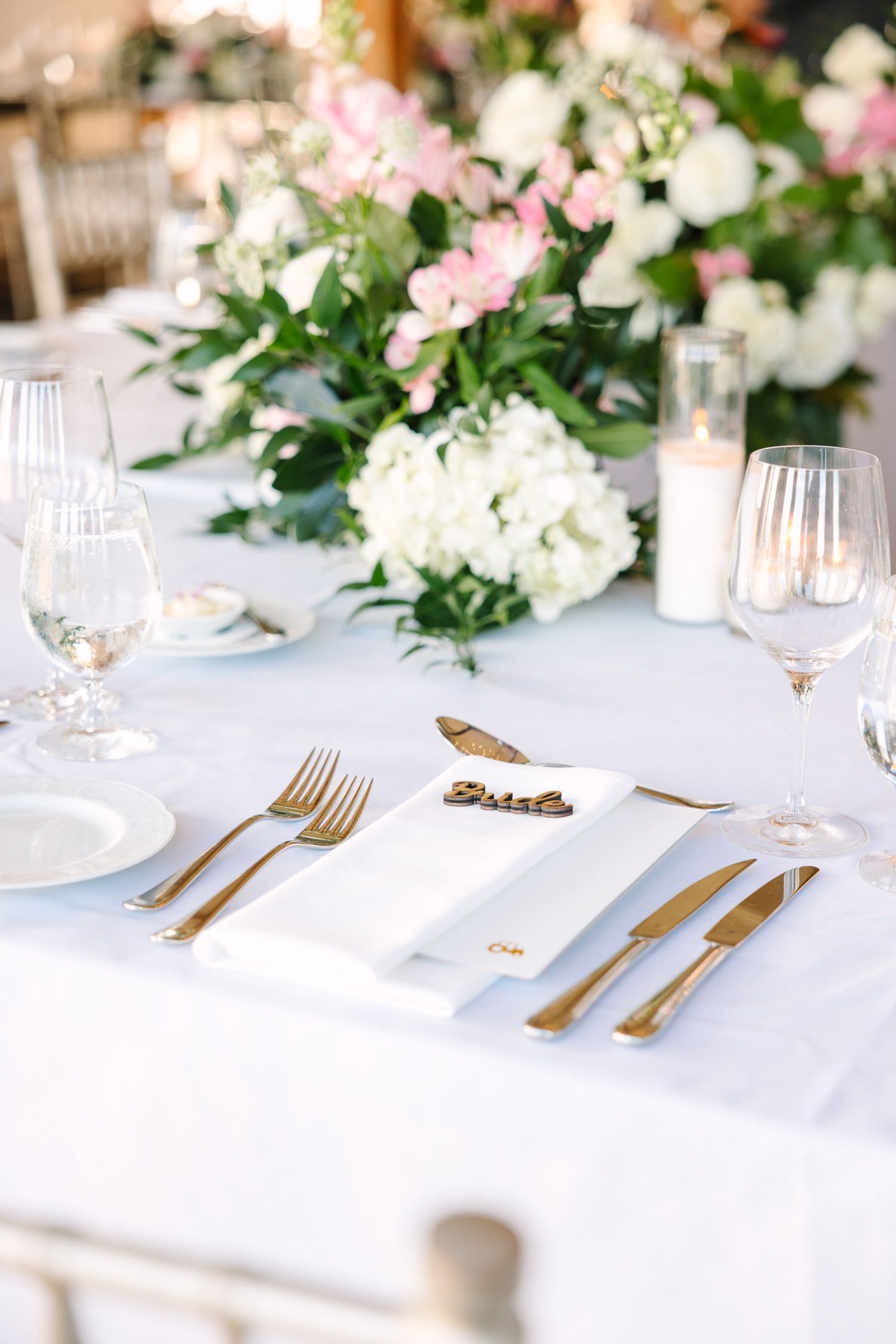 Formal place setting with gold flatware and delicate floral arrangements on white linens.