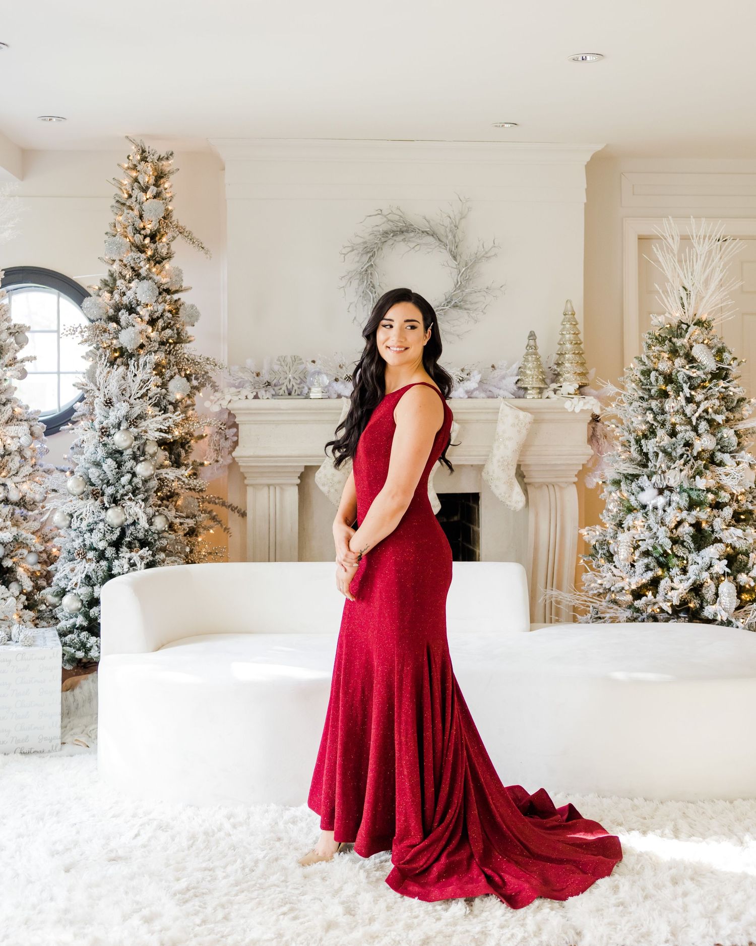 Stunning portrait of woman in red velvet gown surrounded by snow-dusted Christmas trees.