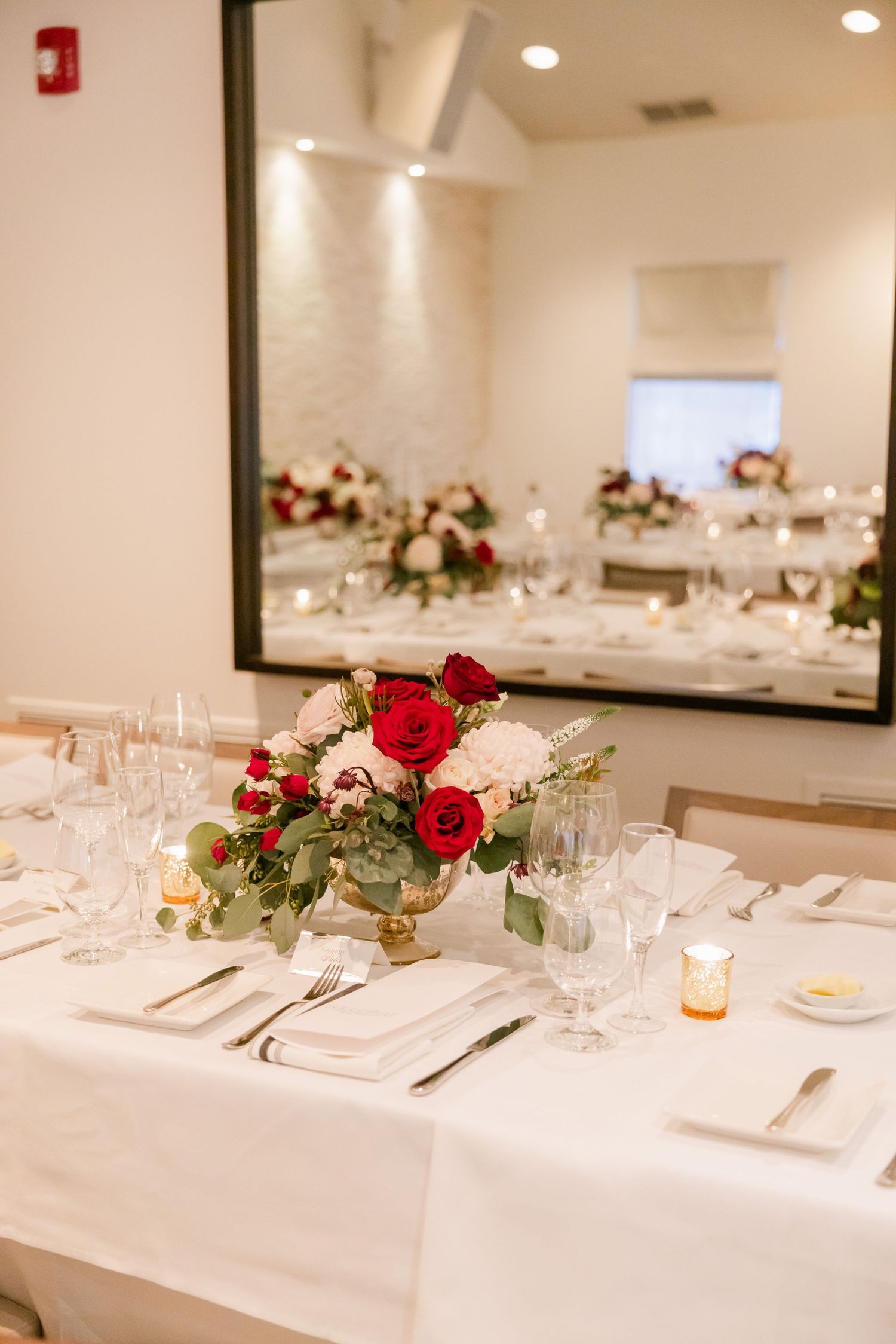 Wedding reception table with red and white roses centerpiece and formal place settings in an elegant room.