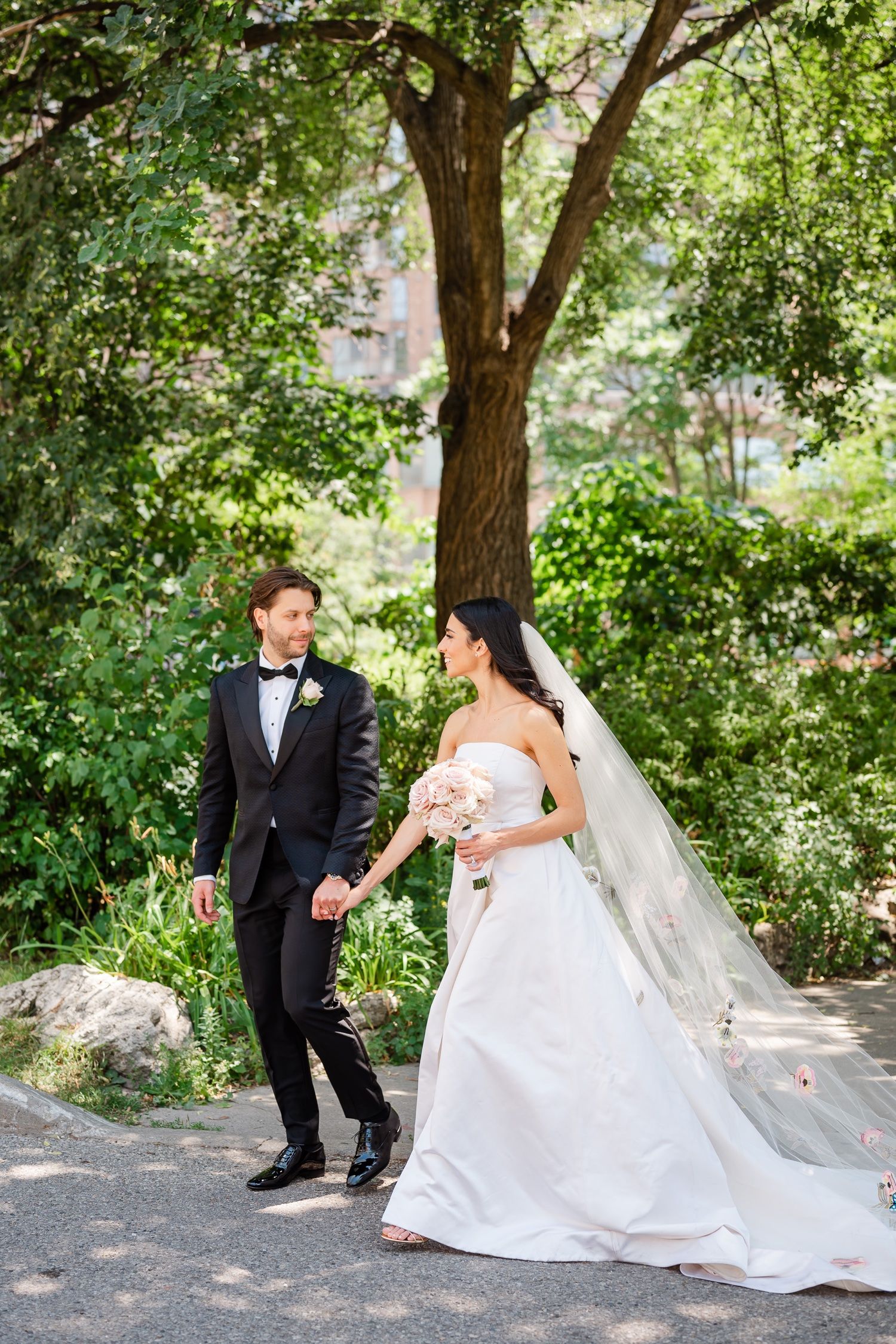 Candid wedding moment captured on garden path with overhanging trees.