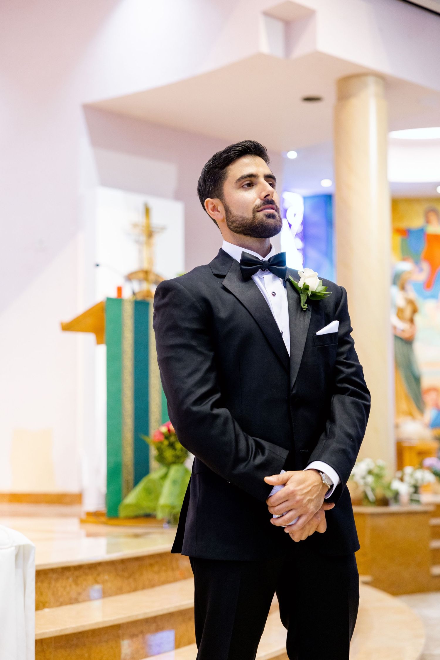 Groom in classic black tuxedo standing in church sanctuary before ceremony.