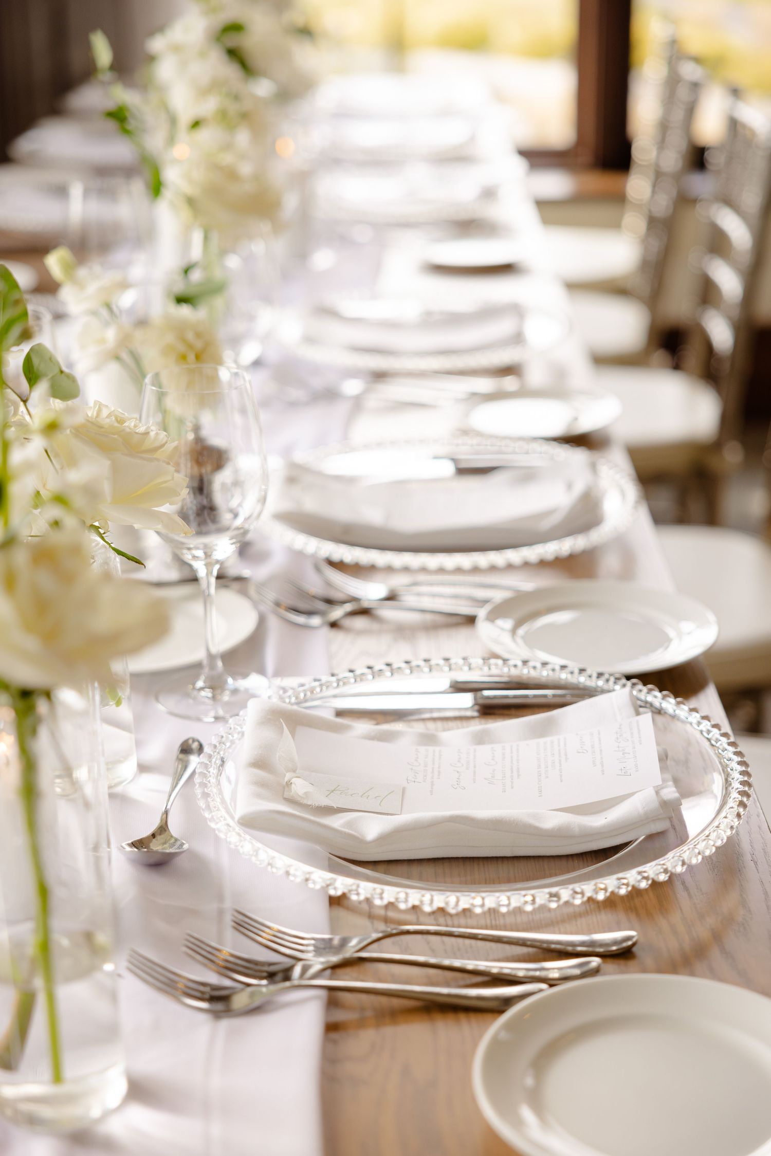 Wedding reception table set with pearl-rimmed charger plates, white linens and delicate floral centerpieces.
