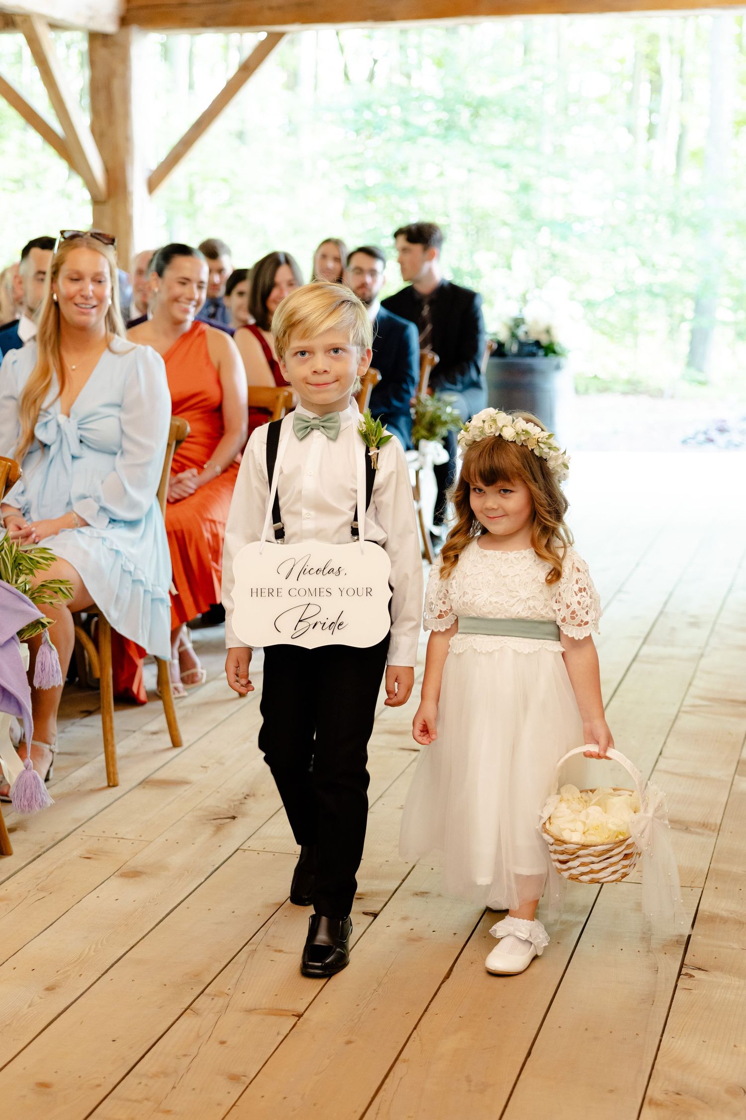 Two children in formal attire walking down a wooden aisle at a wedding ceremony.