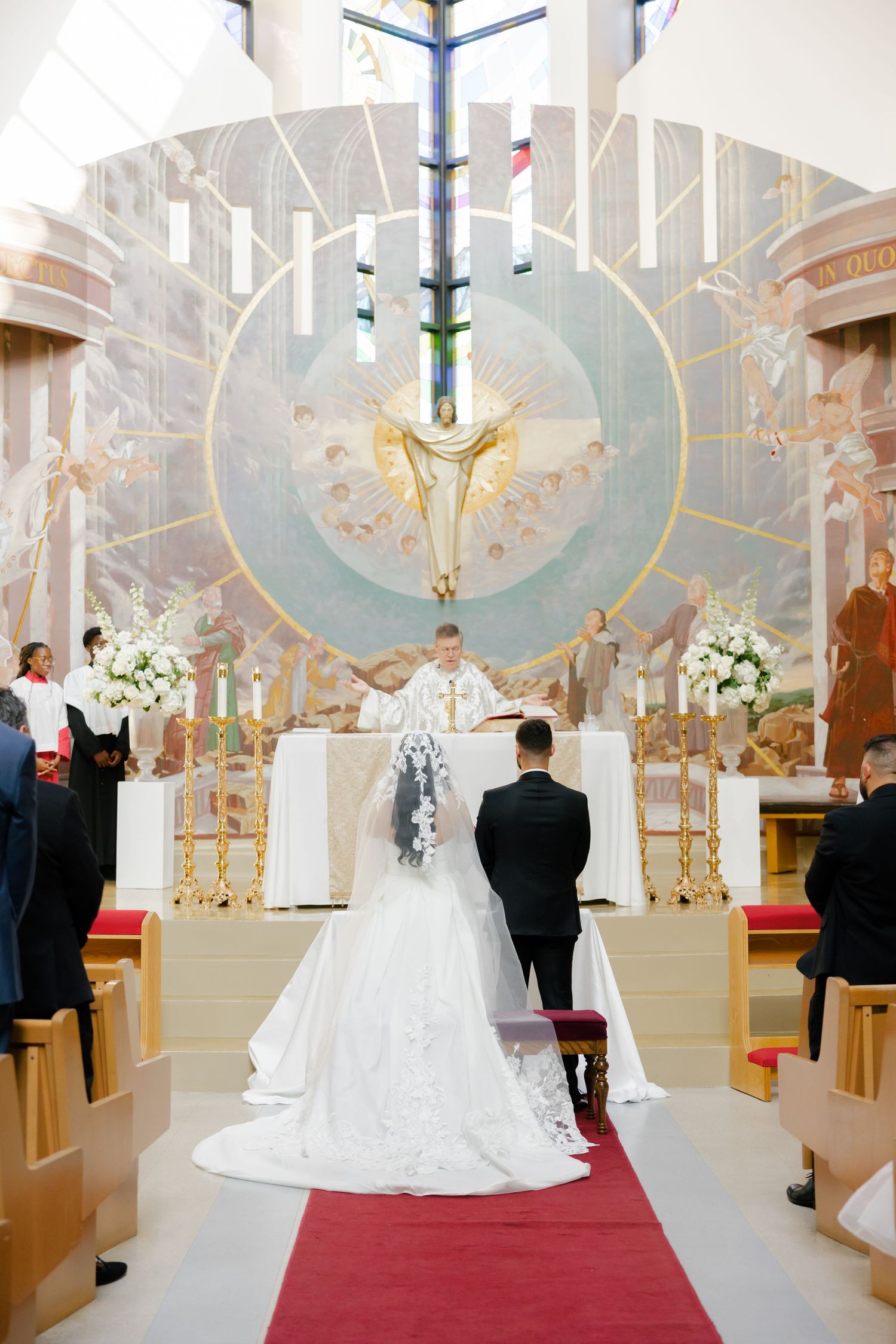 A couple stands at the altar during their wedding ceremony under an ornate church ceiling.