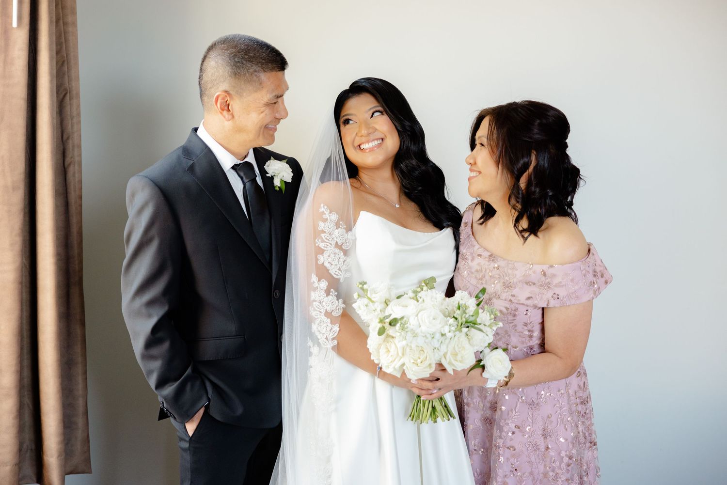 Intimate wedding portrait with wedding party members in formal attire against light wall.