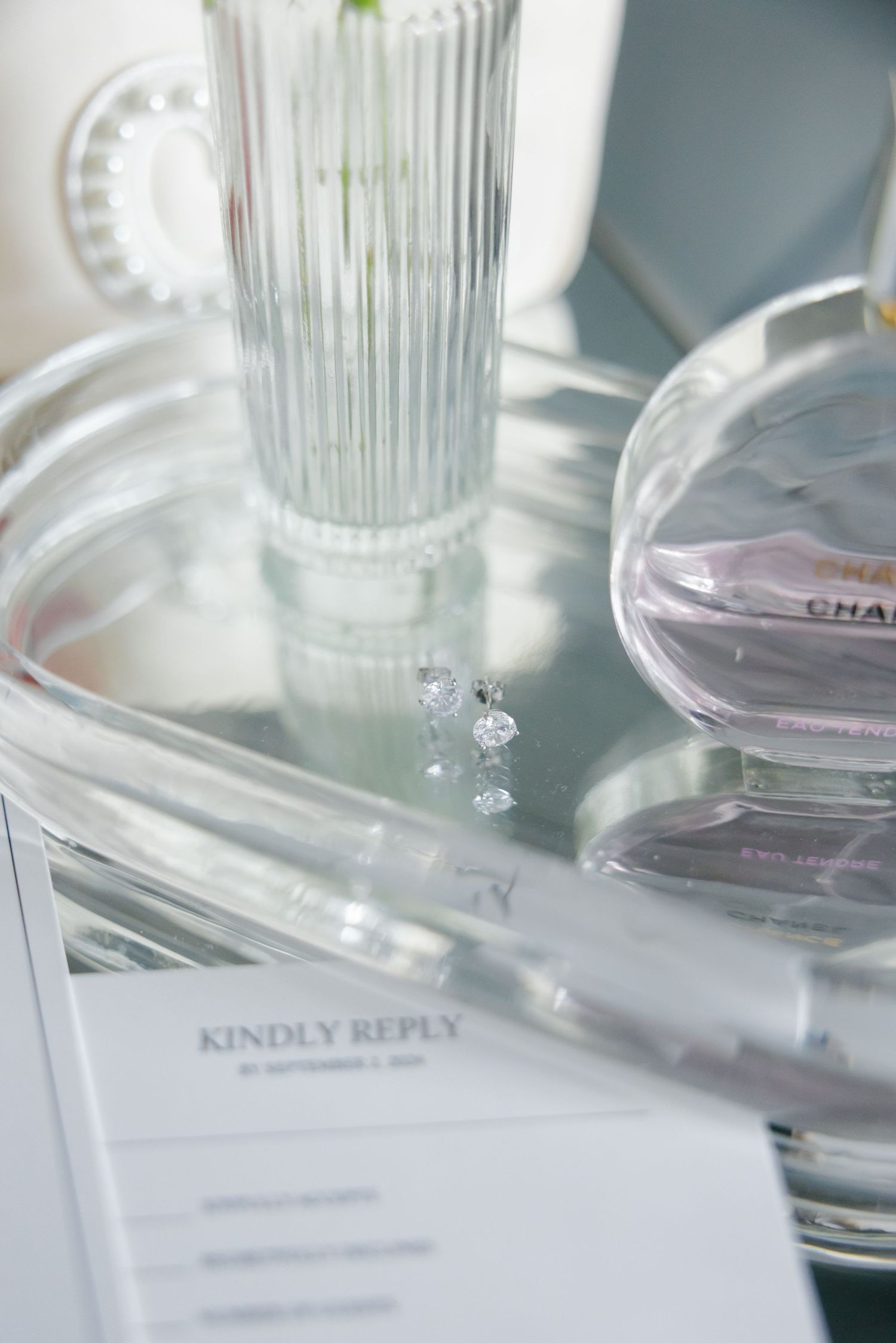 Wedding invitation RSVP card with Chanel perfume and crystal vase on mirrored surface.
