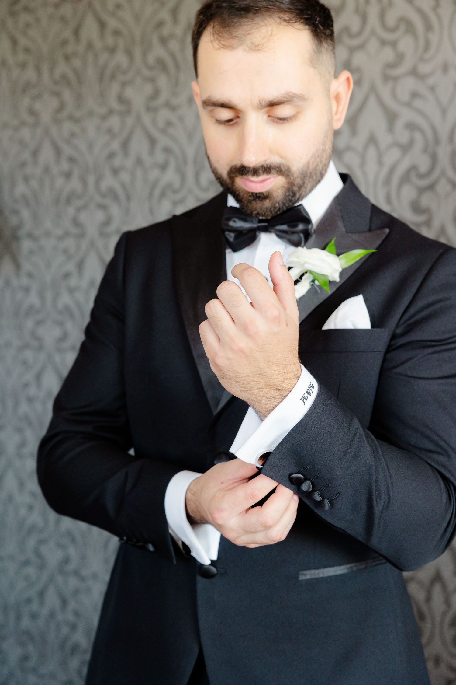 Groom adjusting cuff of tuxedo with white boutonniere.