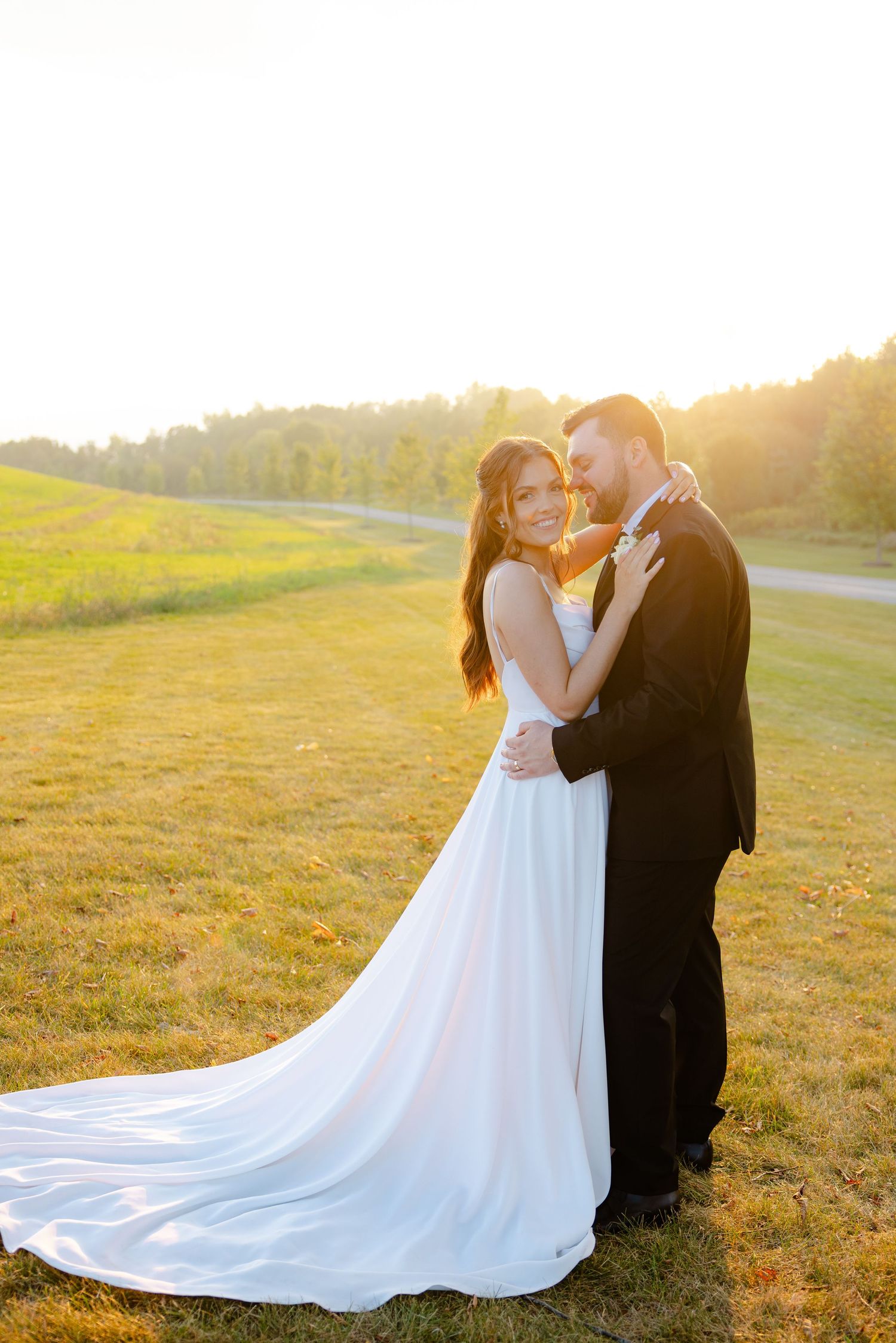 Golden hour wedding portrait features couple in elegant attire against scenic natural backdrop.