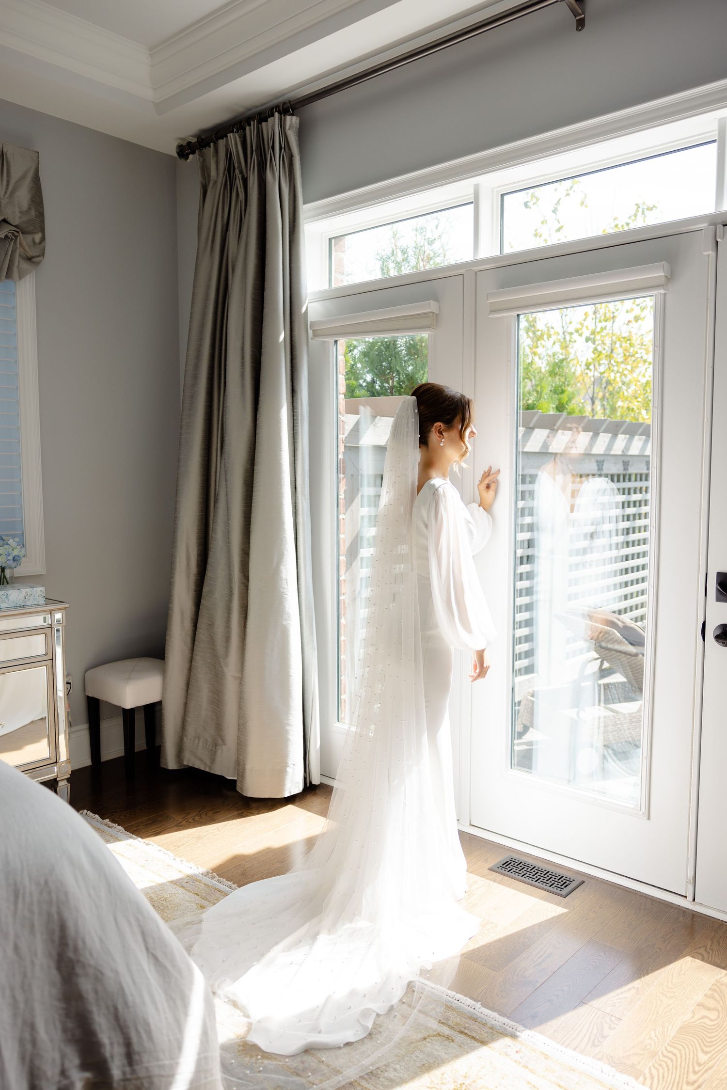 A wedding gown with a flowing train photographed against French doors in natural light.