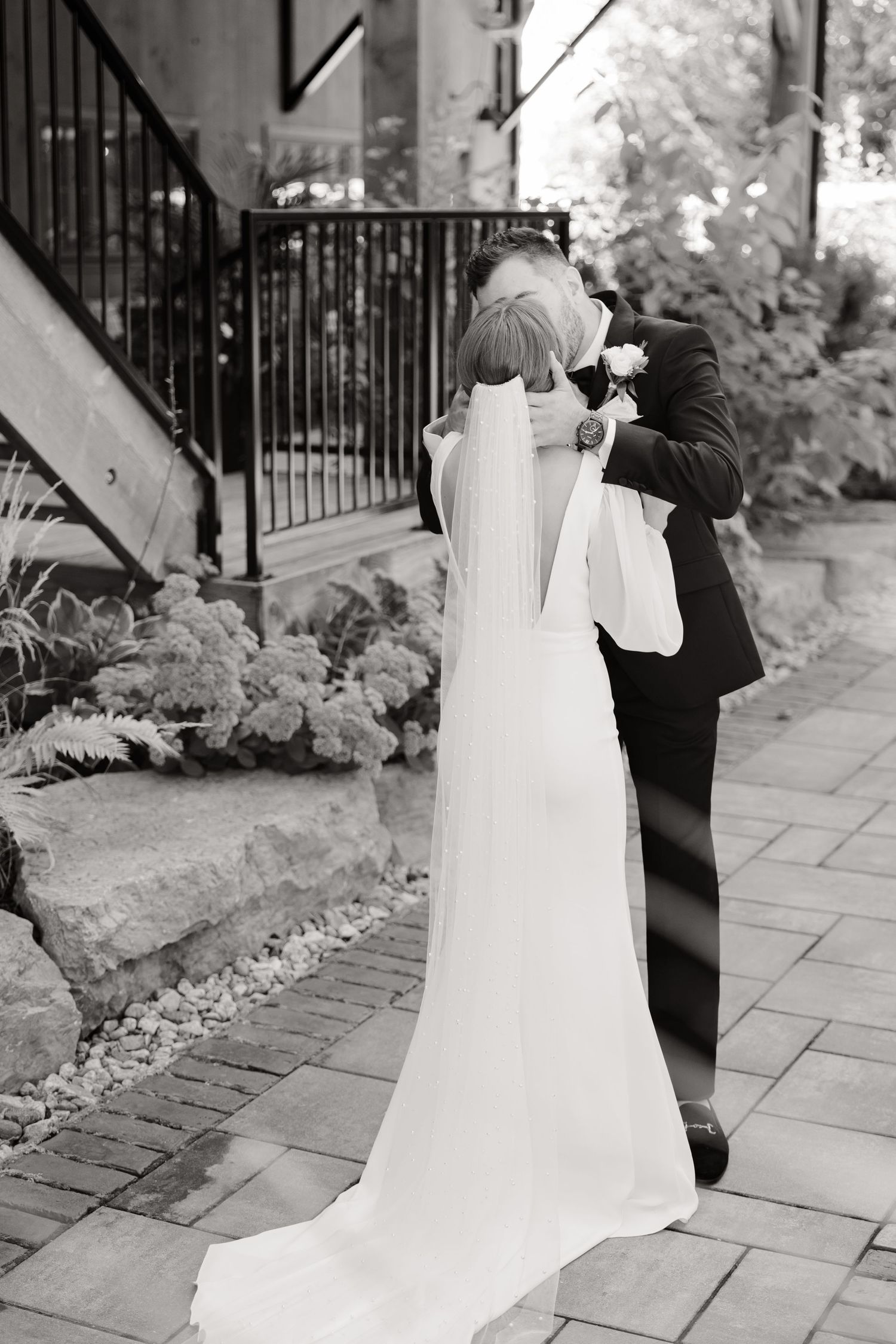 Black and white photograph of newlyweds sharing a romantic moment on a garden pathway.