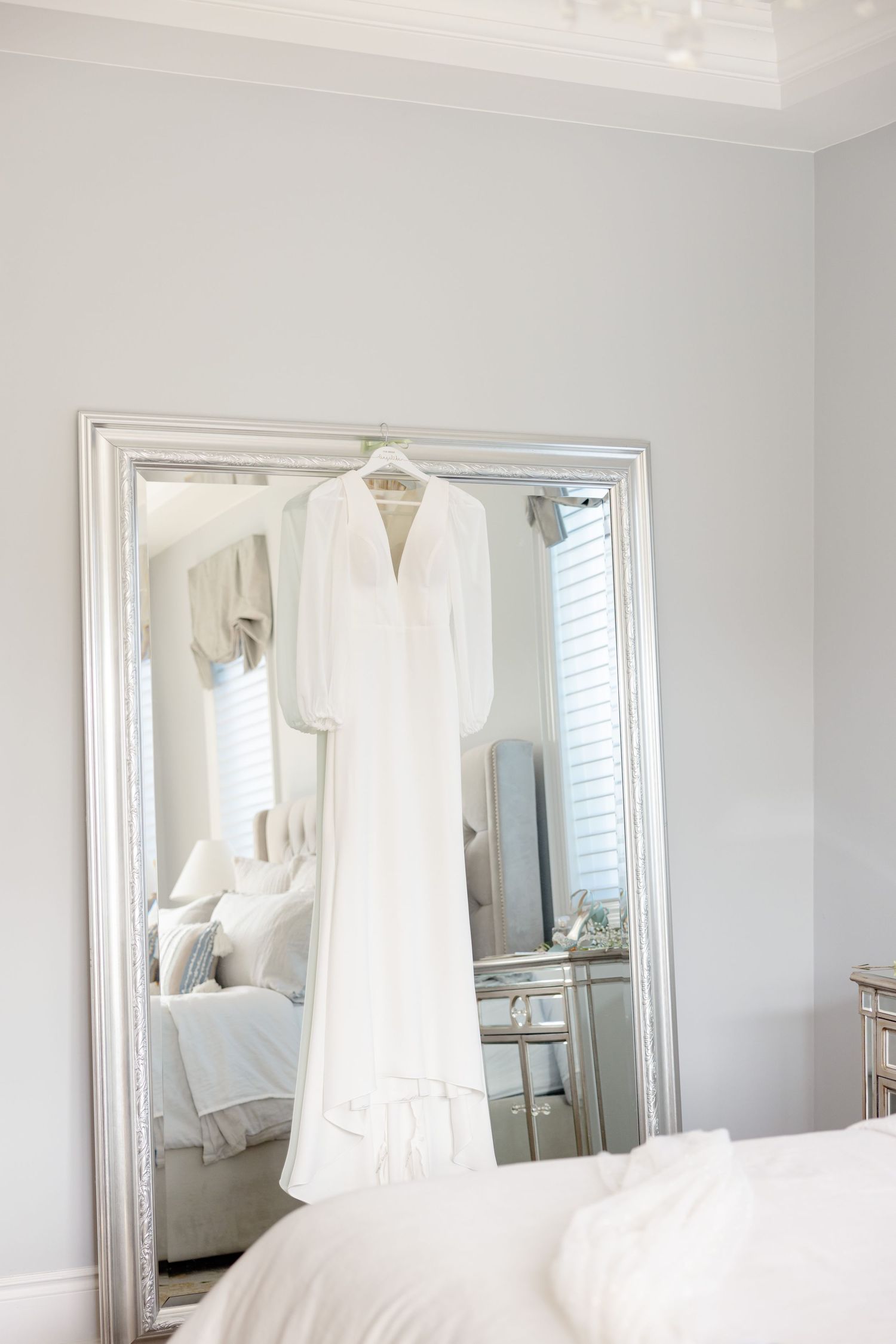 White wedding gown hanging on display in front of a large mirror in a bright room.
