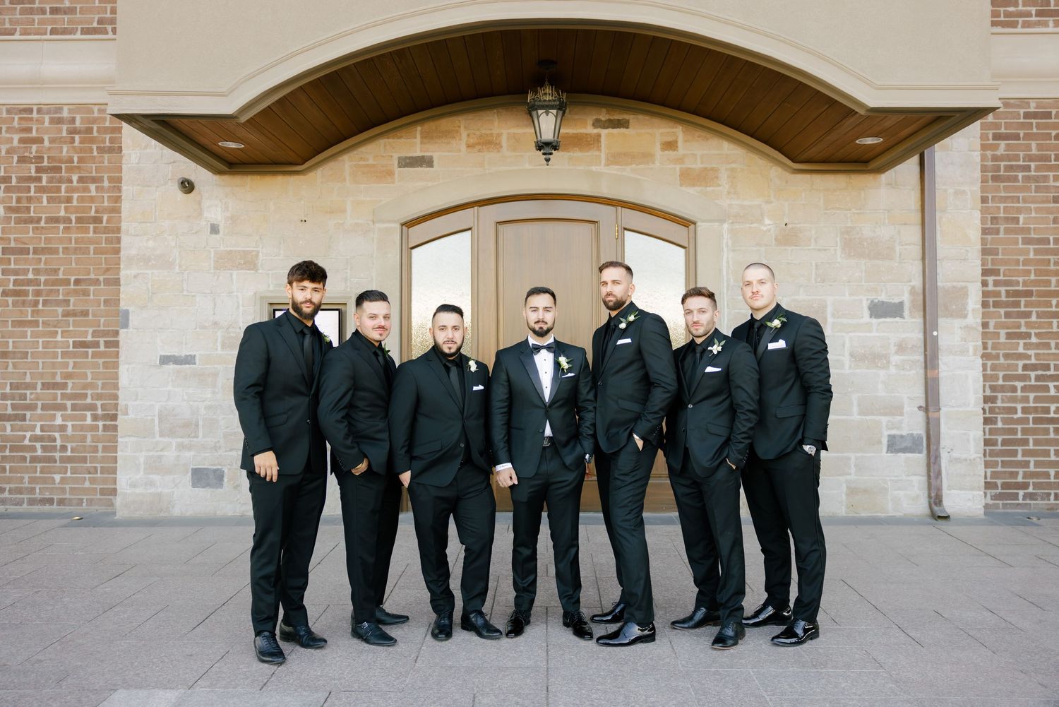 Wedding party members in matching black suits stand in formation for a formal portrait.