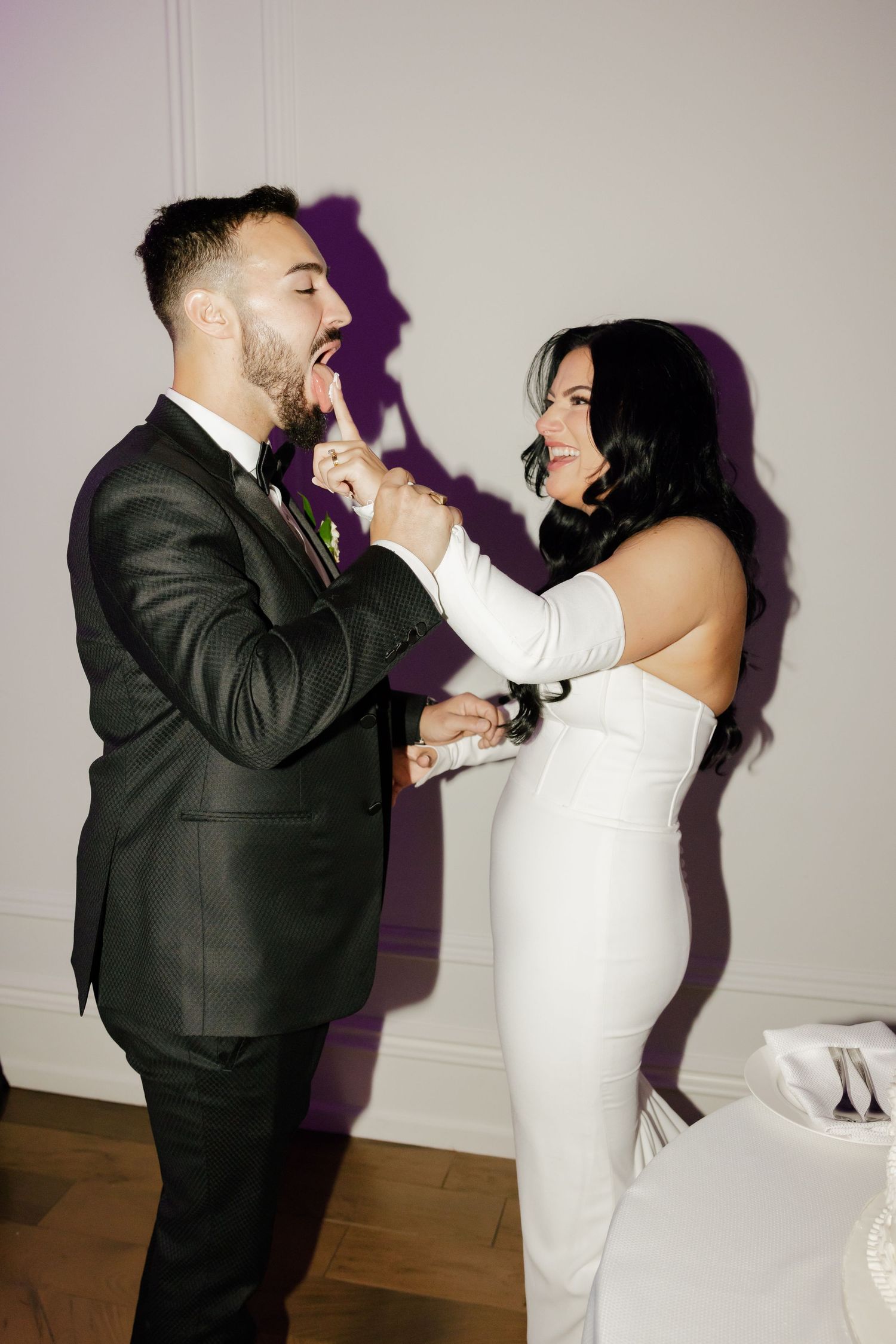 Playful moment between newlyweds feeding each other cake at their wedding reception.
