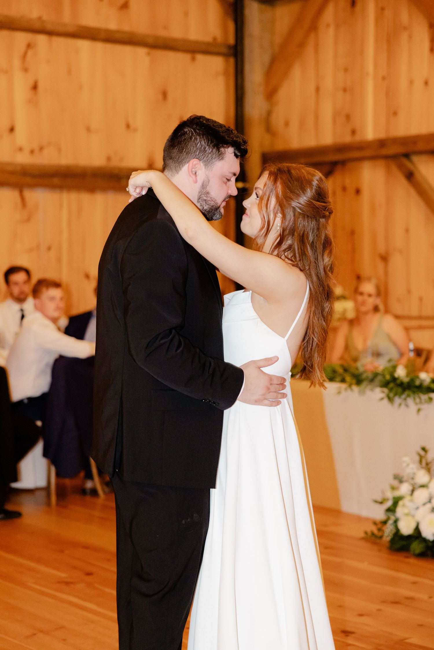 Intimate dance moment between couple in elegant attire within a wooden barn reception space.