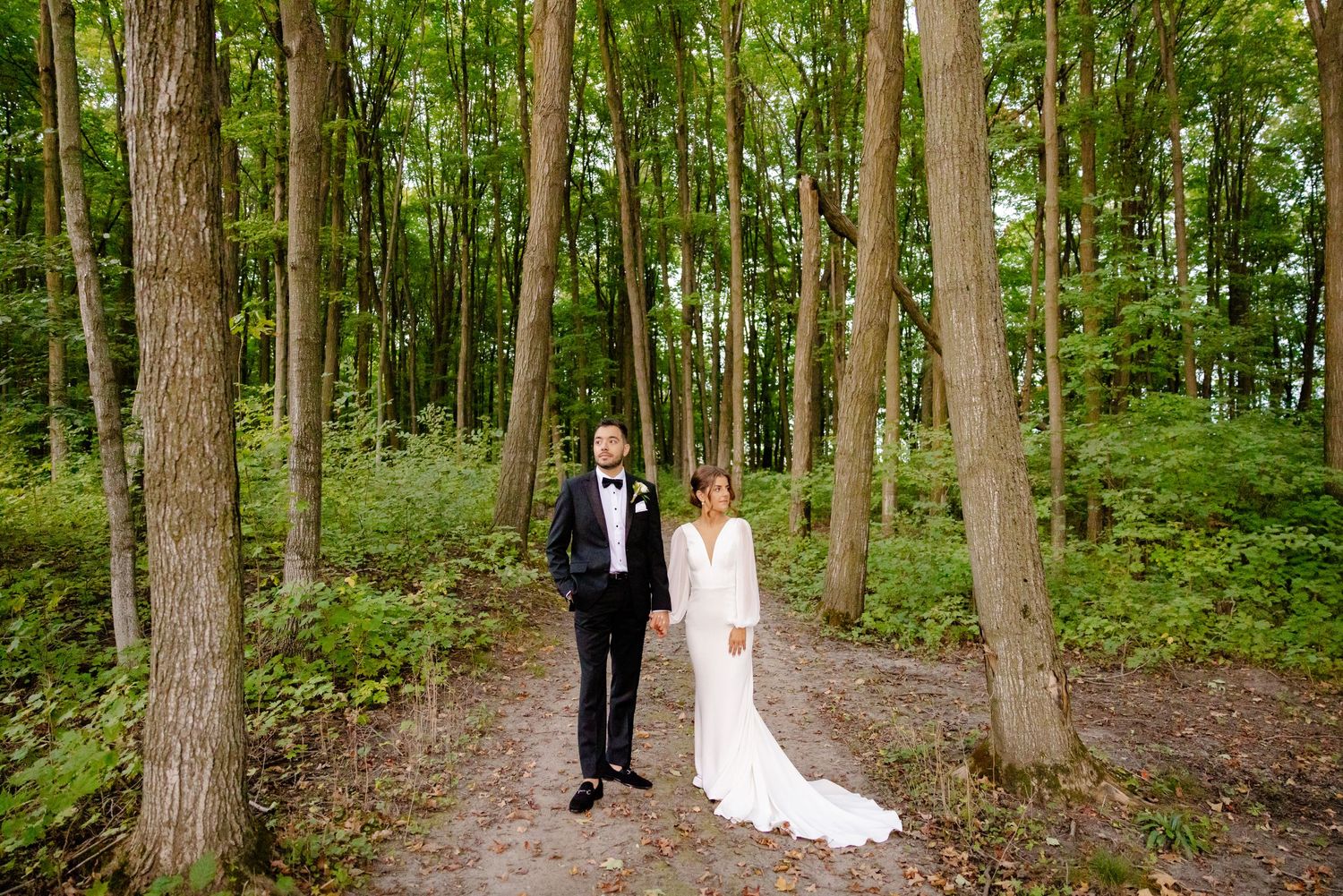 A formal wedding portrait of a couple on a wooded trail surrounded by green trees.