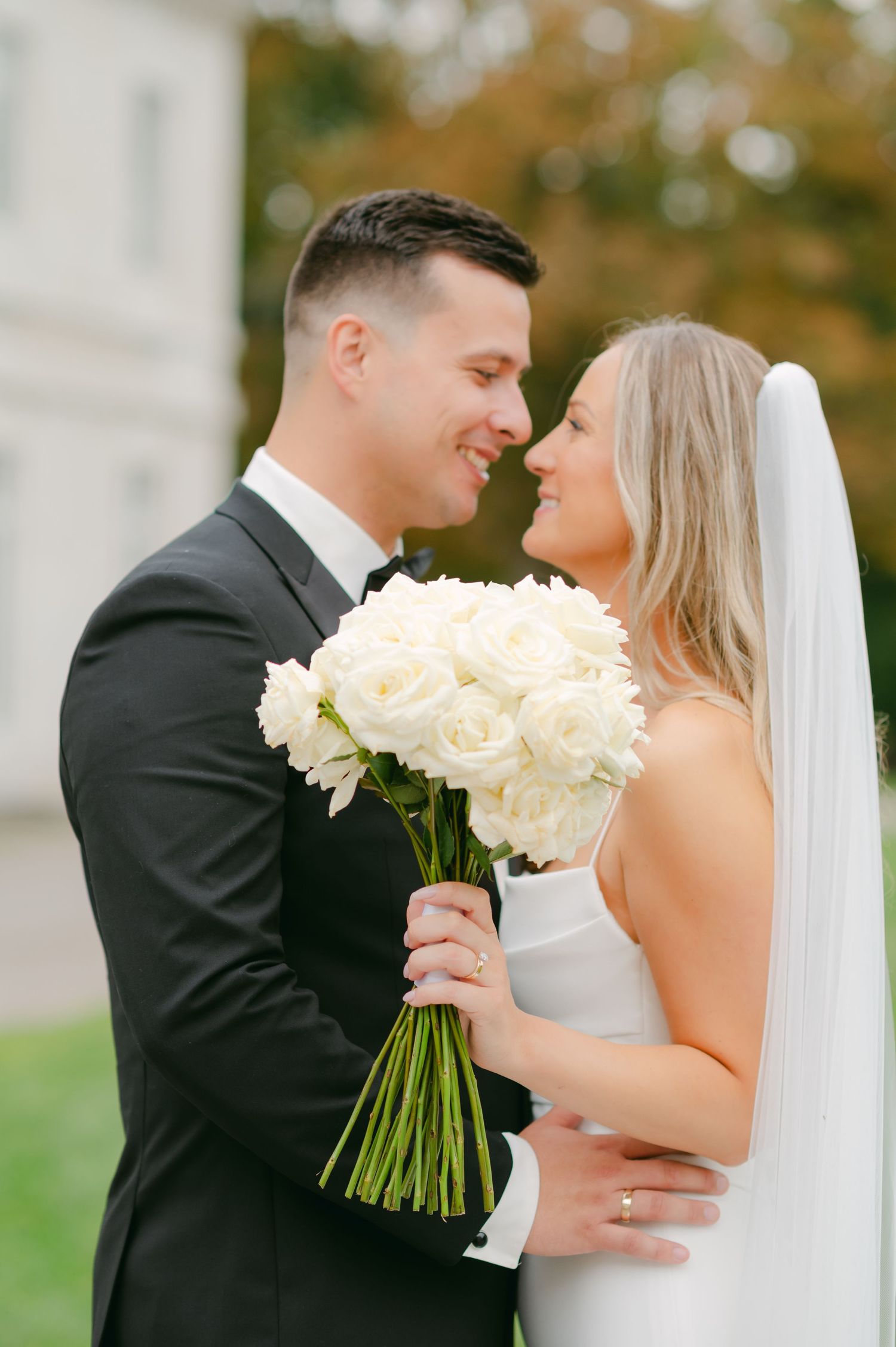 Intimate wedding portrait with couple sharing moment while holding white rose bouquet.