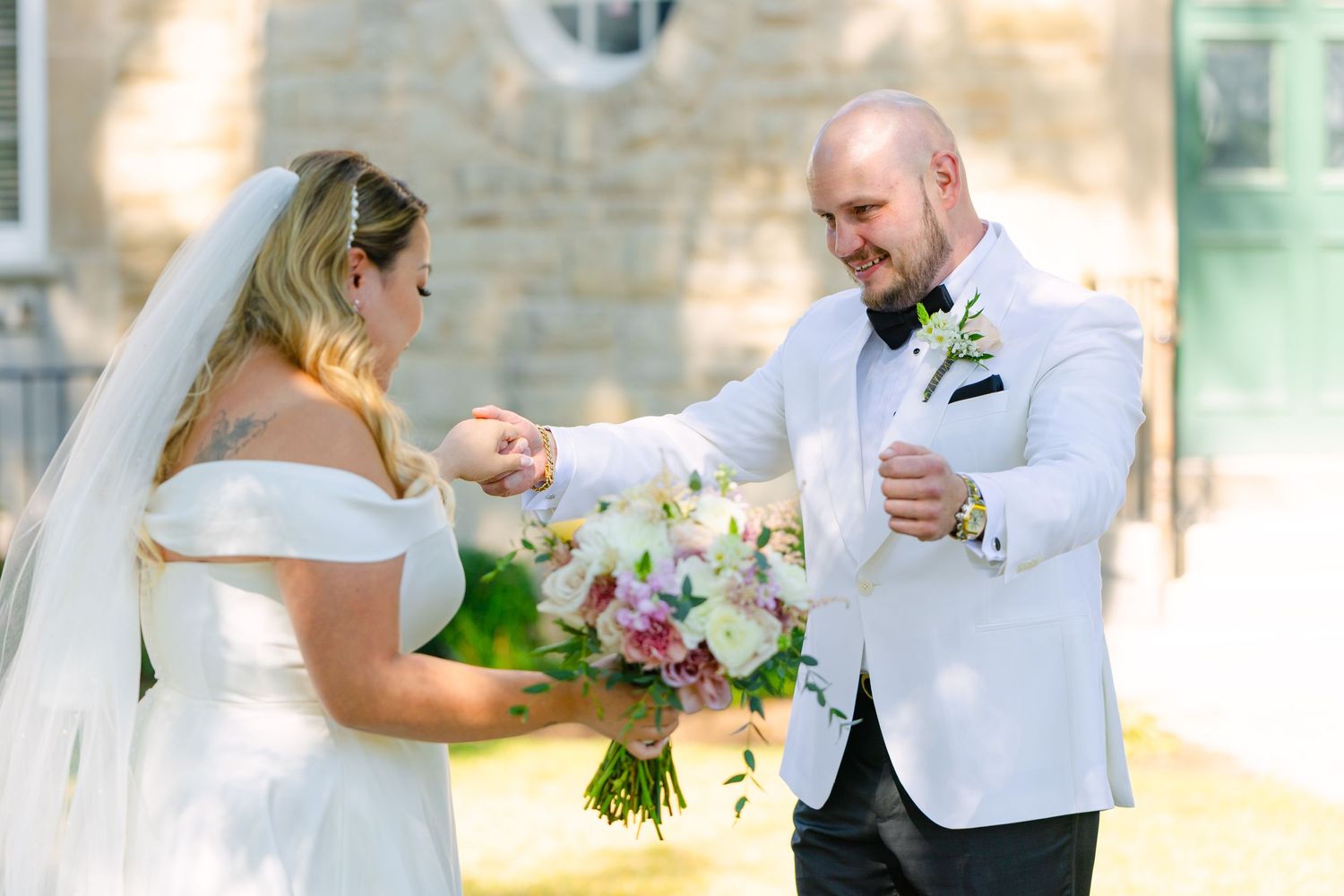 Joyful wedding reactions captured in bright sunlight with stone building backdrop.