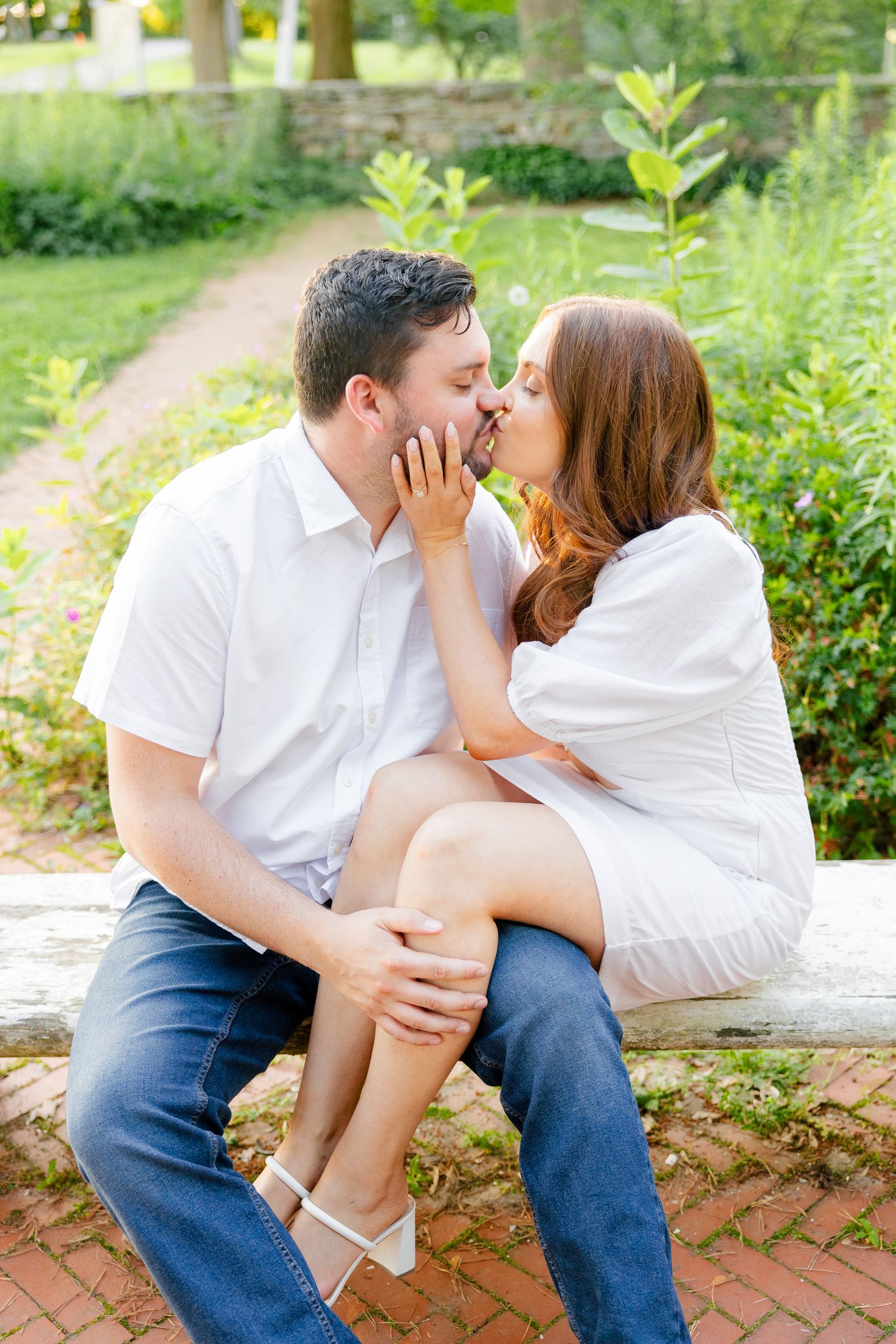 An intimate portrait of a couple sharing a romantic moment on a stone bench surrounded by greenery.