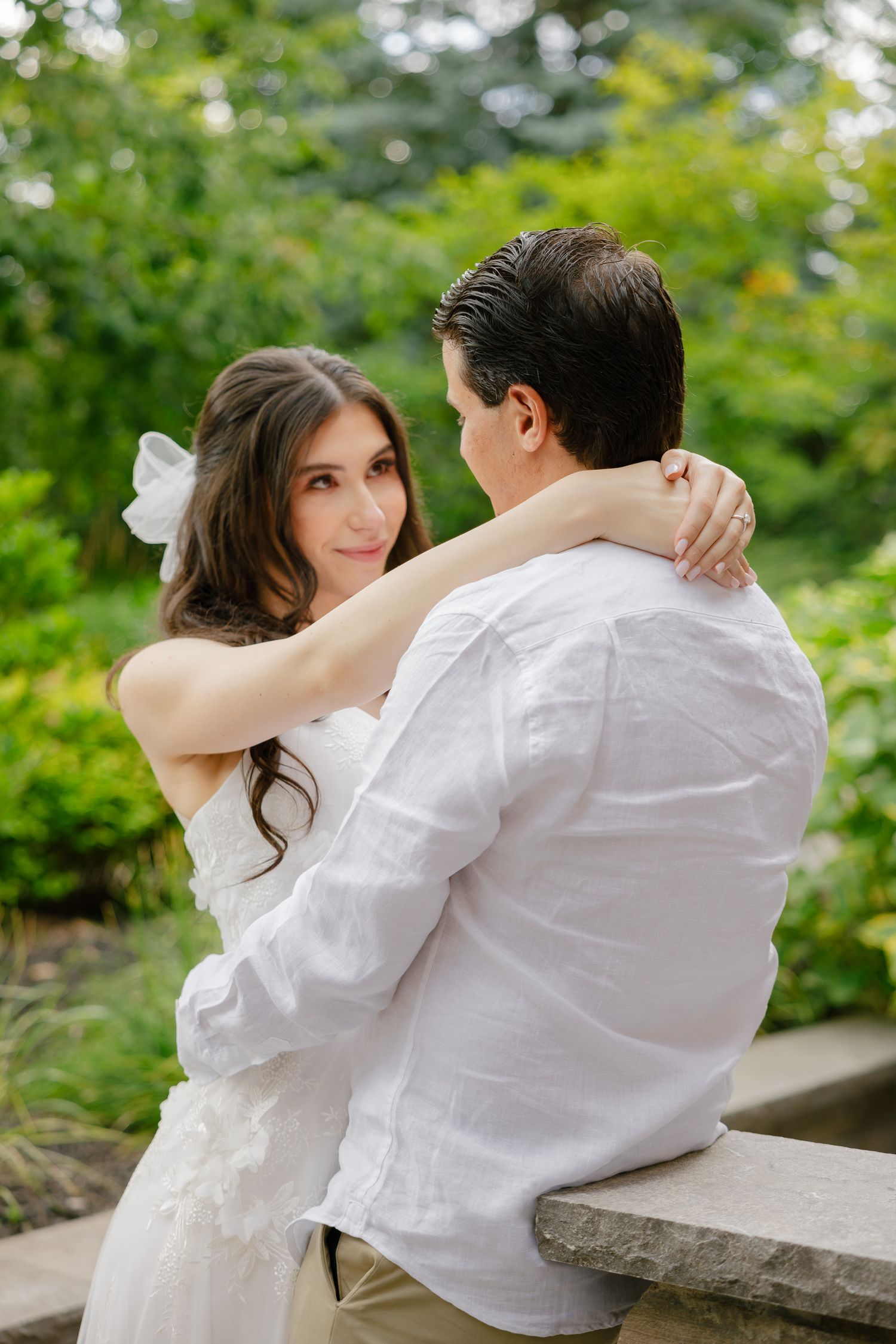 Bride in a lace gown and groom in white share an intimate moment in a garden setting.
