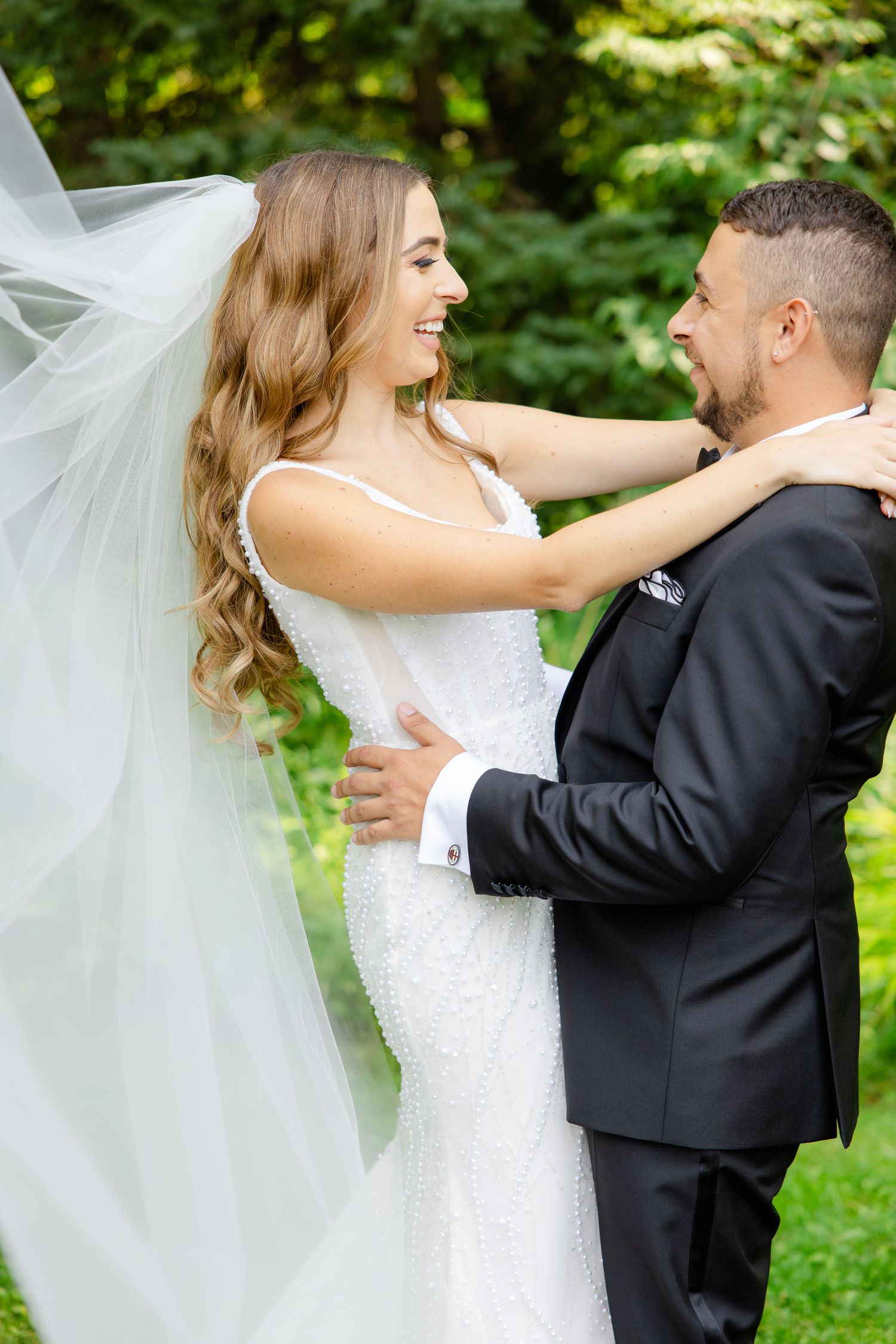 A joyful wedding portrait showing a happy couple embracing against a verdant forest backdrop.