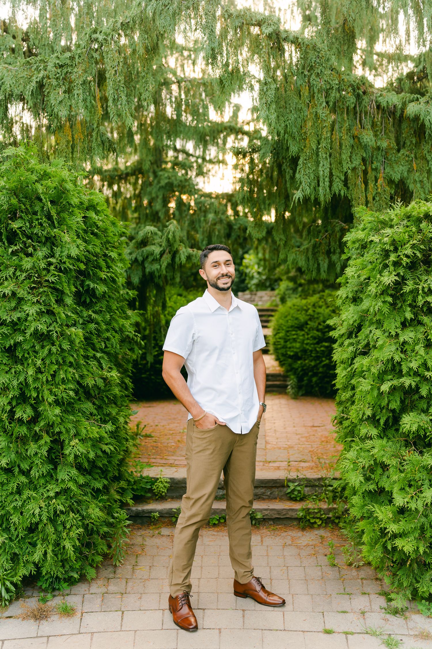 A garden walkway framed by evergreen shrubs and willow trees creates a romantic setting.