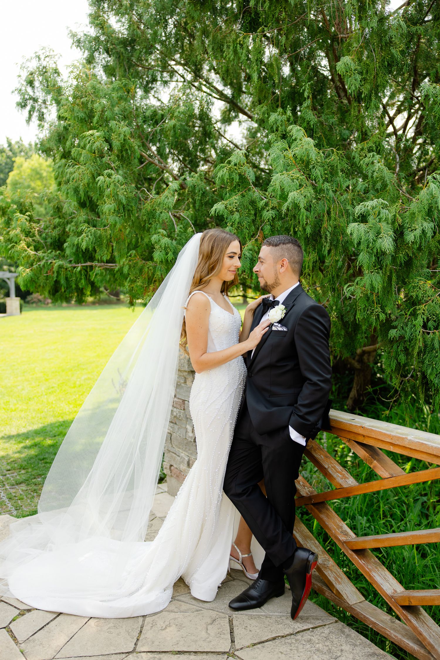 Elegant couple poses by rustic wooden fence with flowing wedding dress and veil.