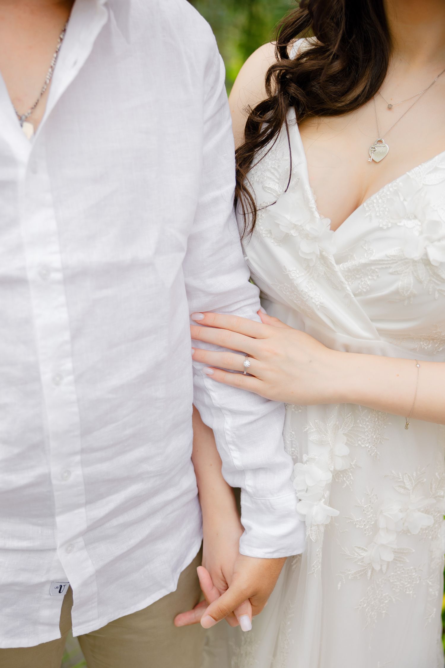 Detail shot of wedding attire and hands showing the bride's ring against white clothing.